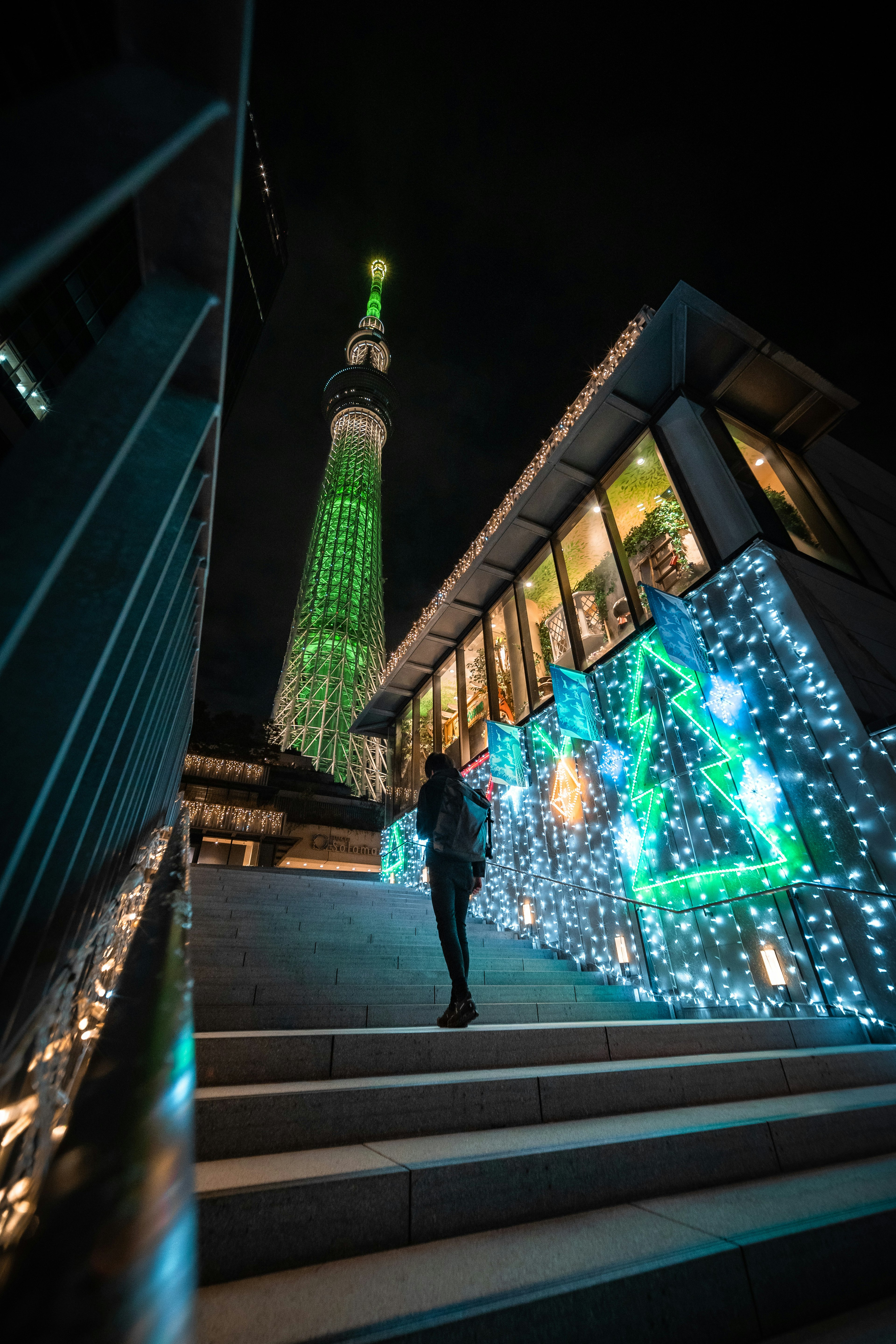 Menara Tokyo Skytree diterangi lampu hijau di malam hari dengan seseorang menaiki tangga