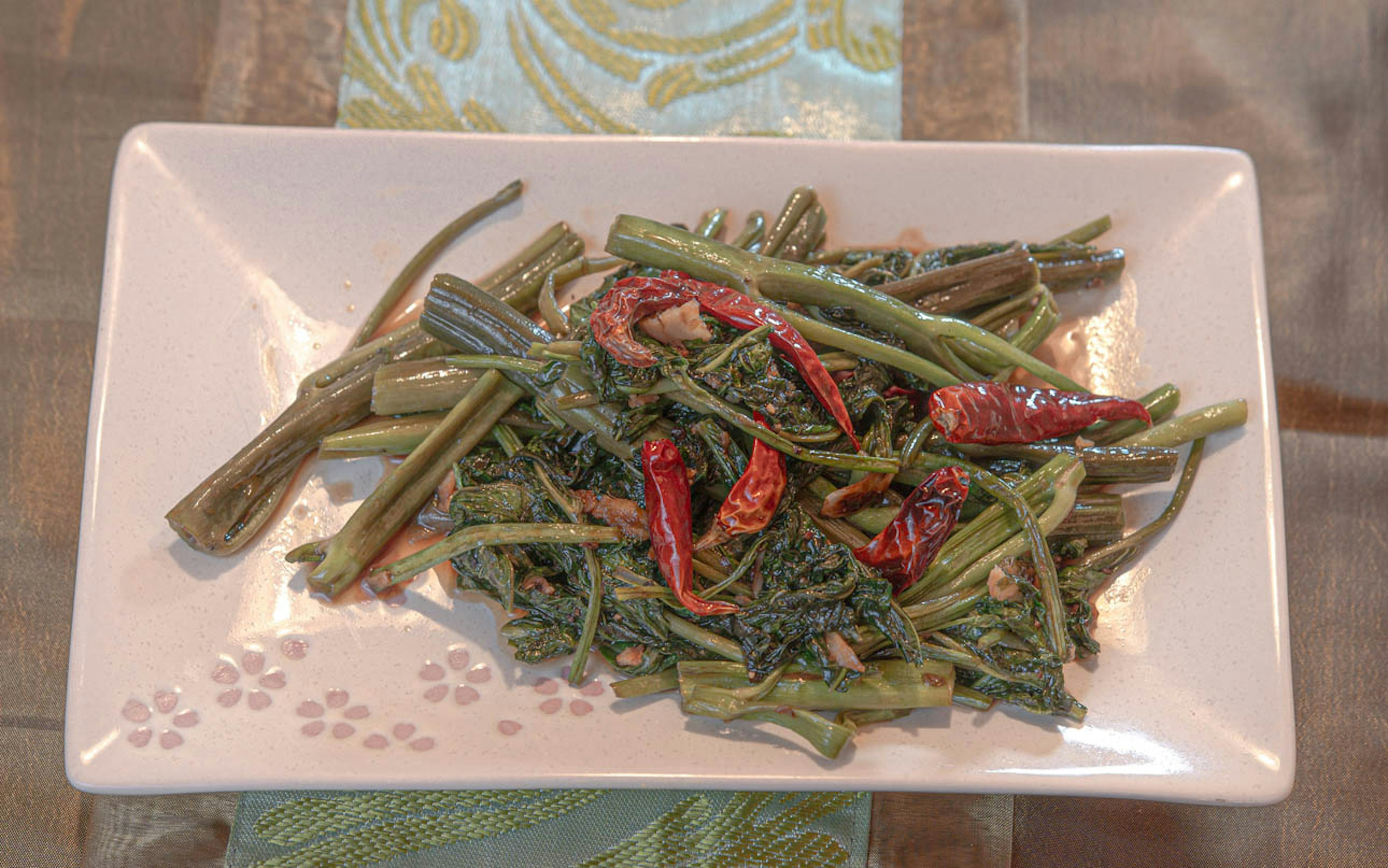 Plate of green vegetables with dried red chilies