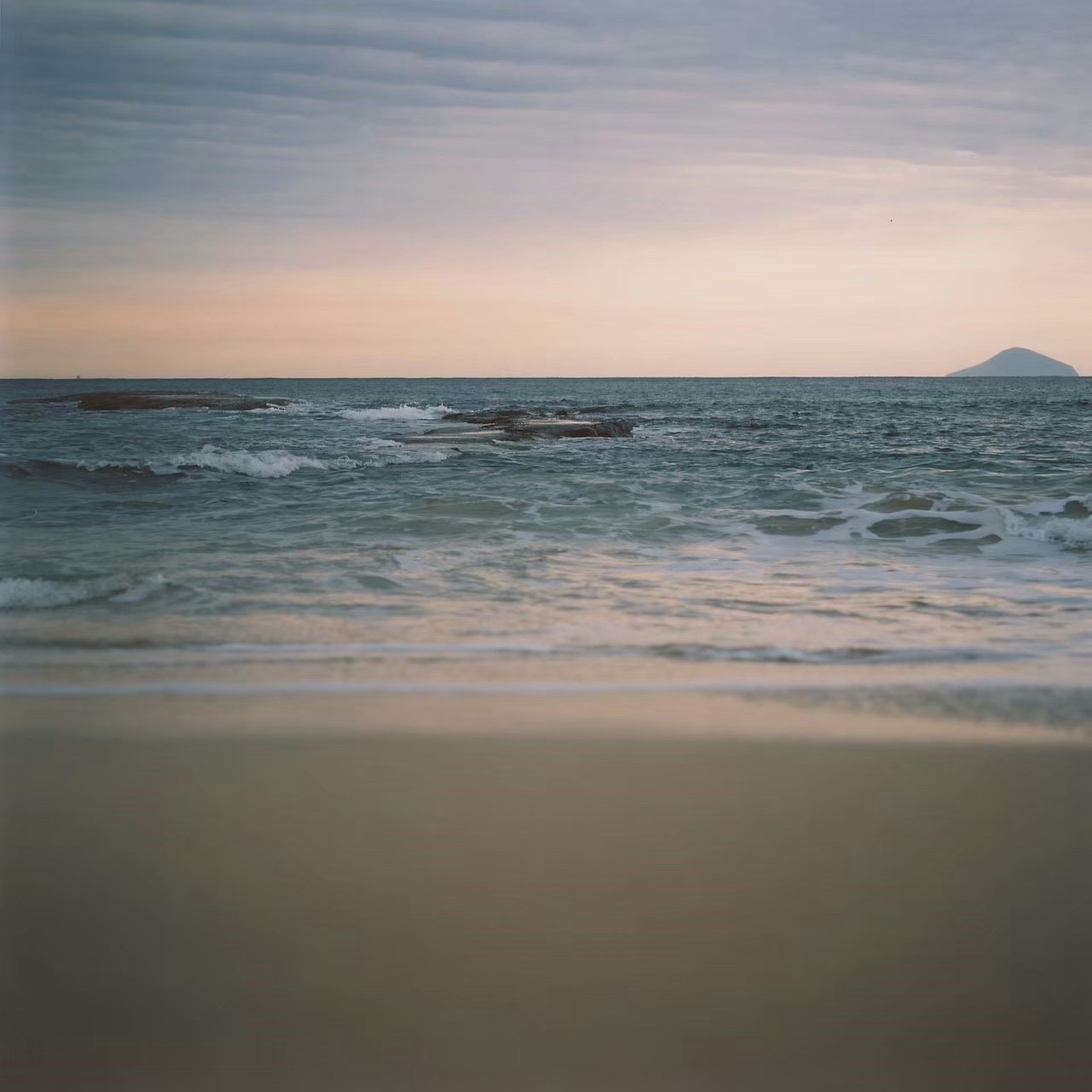 Escena de playa de arena y océano tranquilo con cielo nublado y montaña lejana