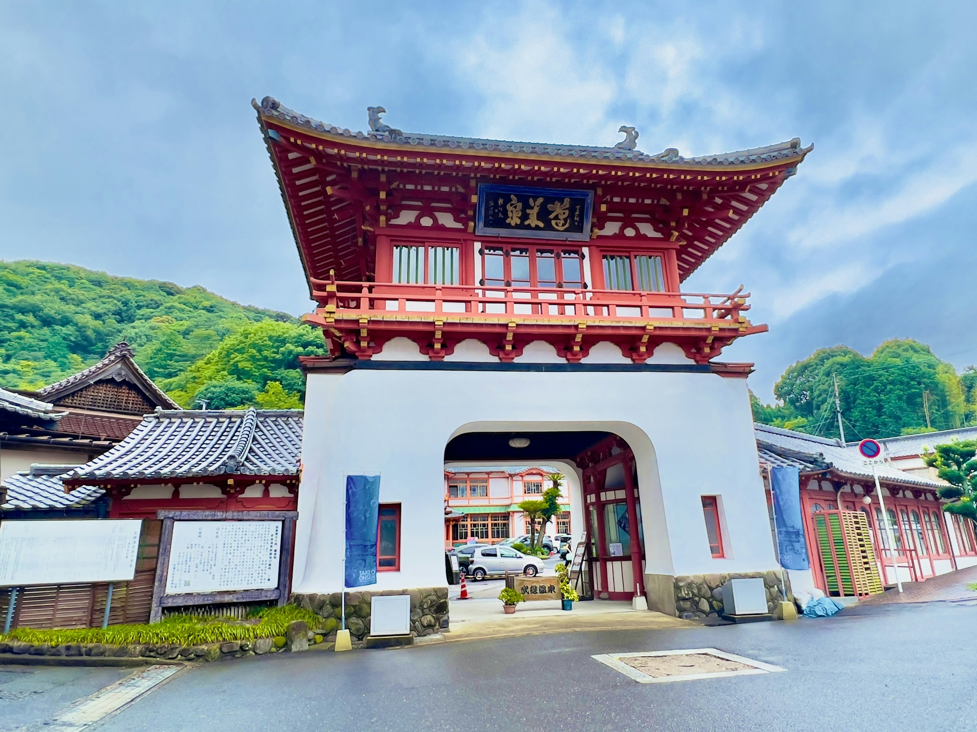 Traditional Japanese architectural gate with red roof and white walls green mountain in the background