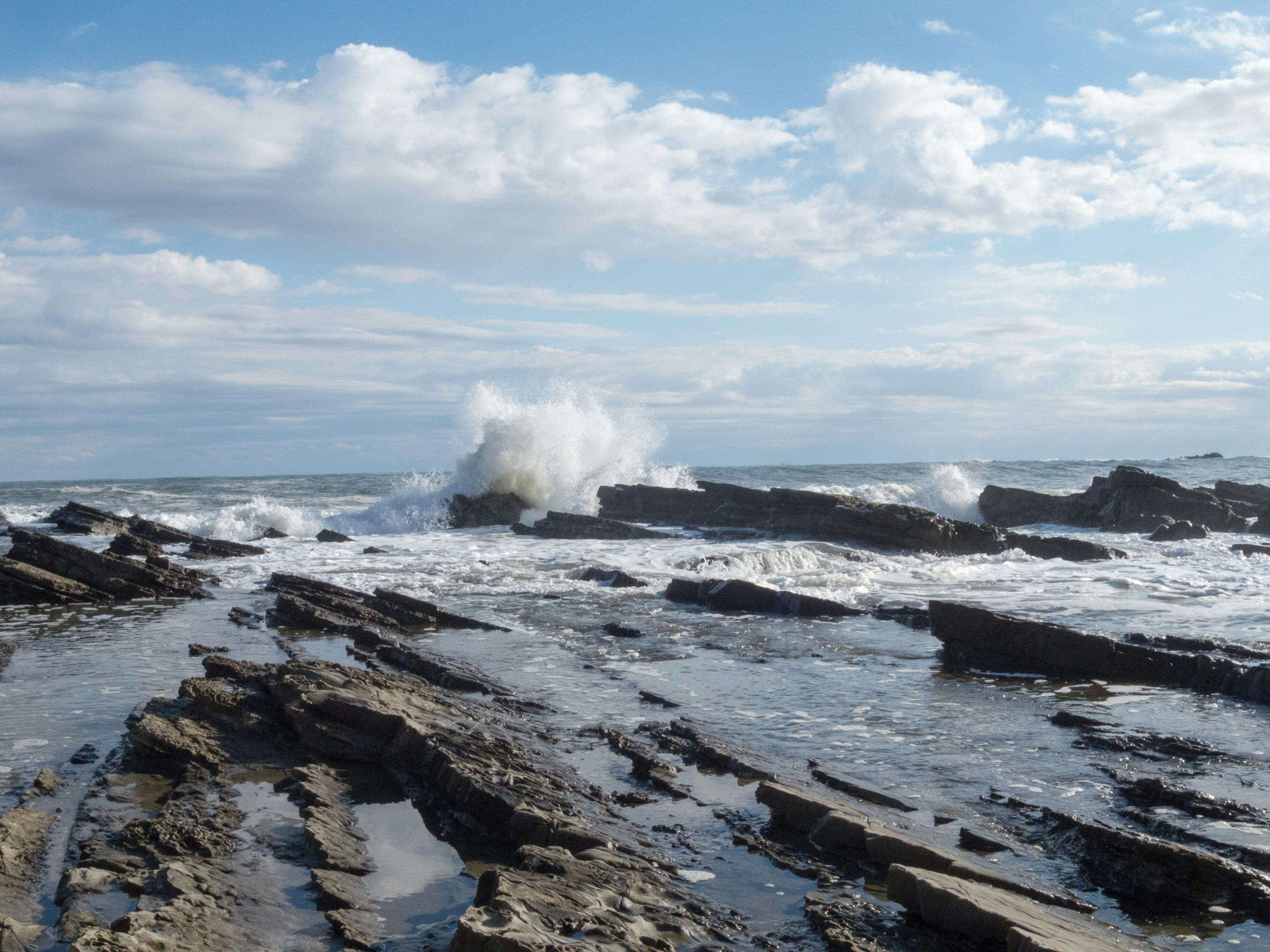 Waves crashing against rocky shoreline under a blue sky