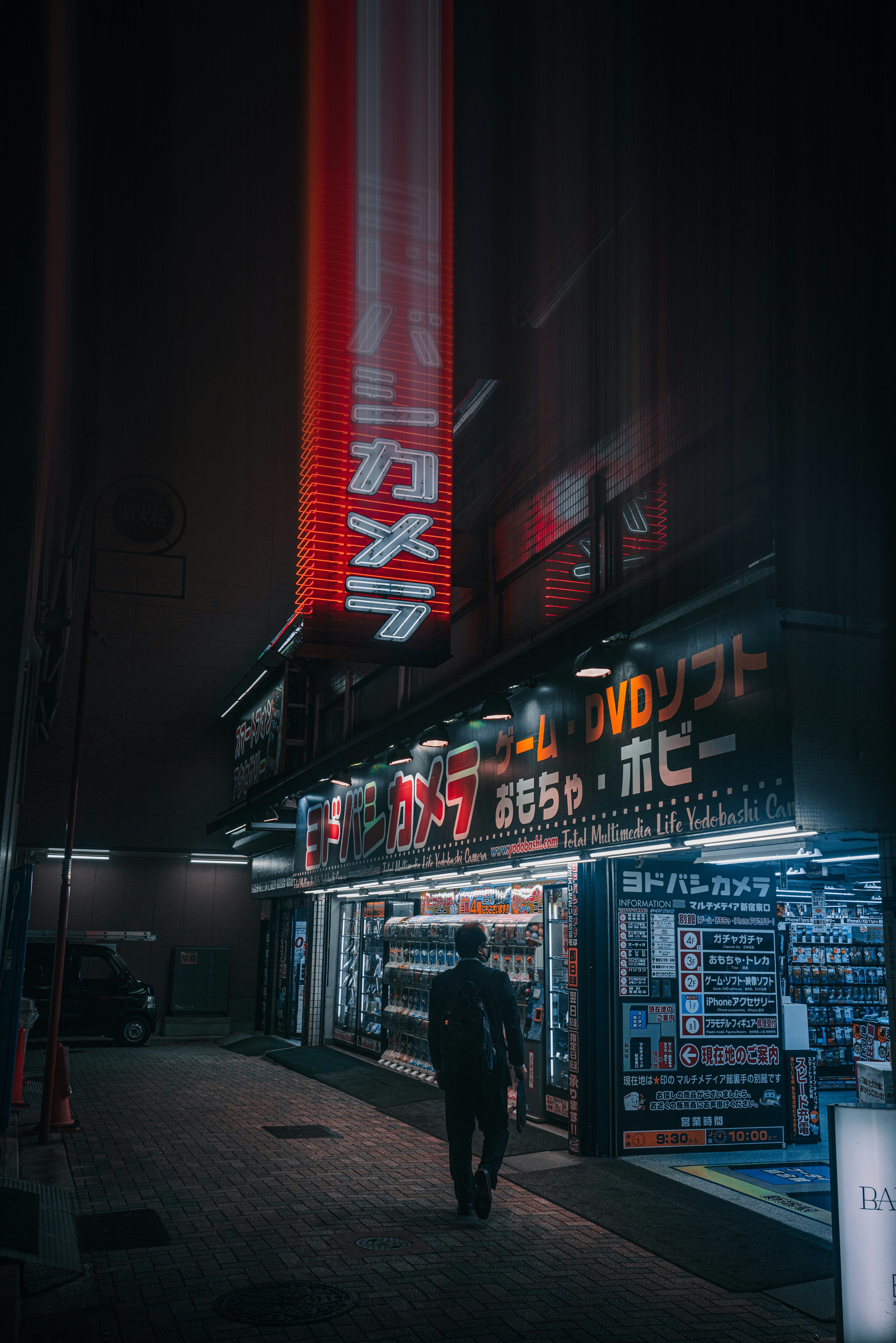 A person walking in a dimly lit street with neon signs and storefronts