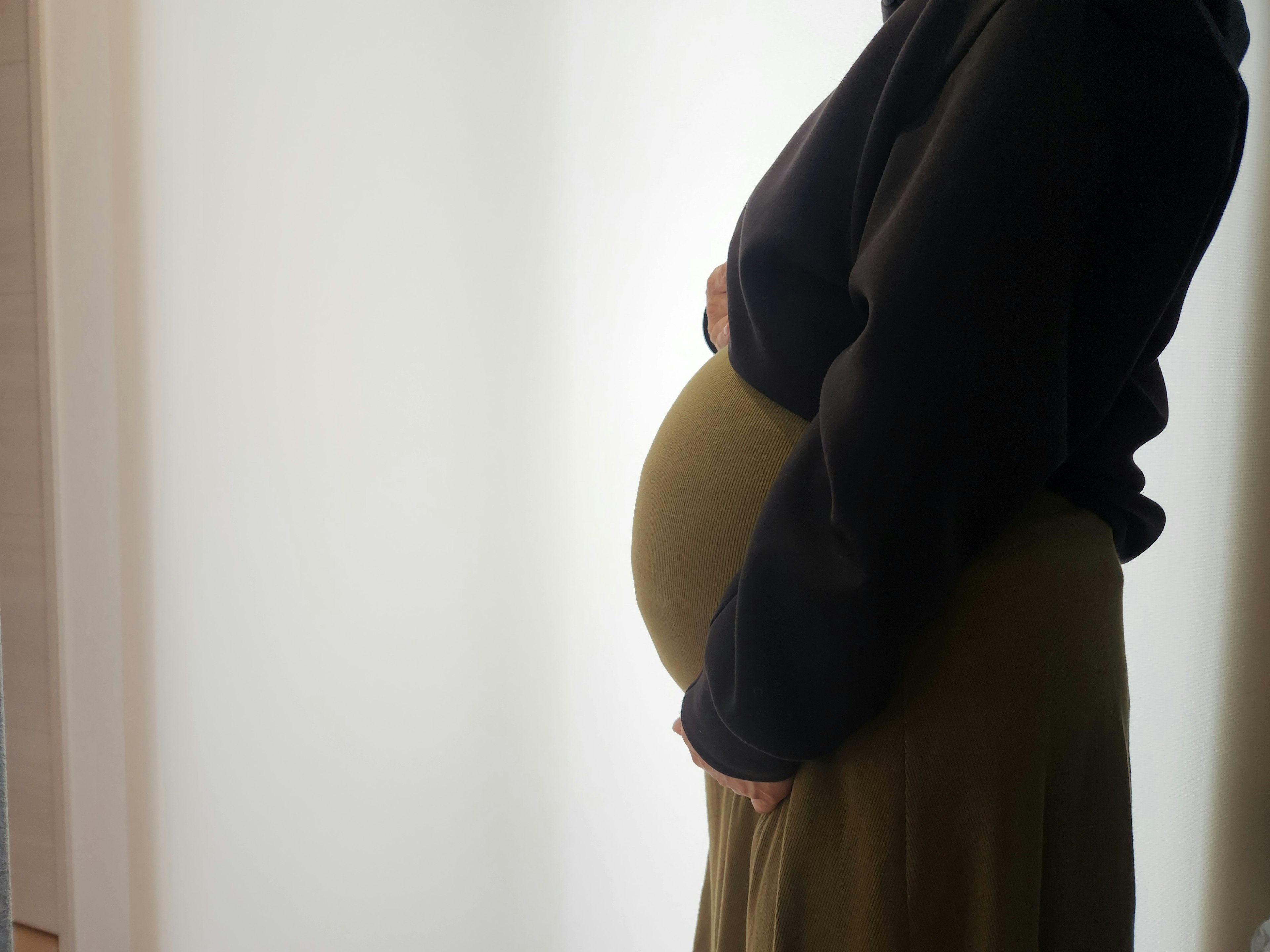 Vue latérale d'une femme enceinte tenant doucement son ventre vêtue d'un sweat noir et d'une jupe verte