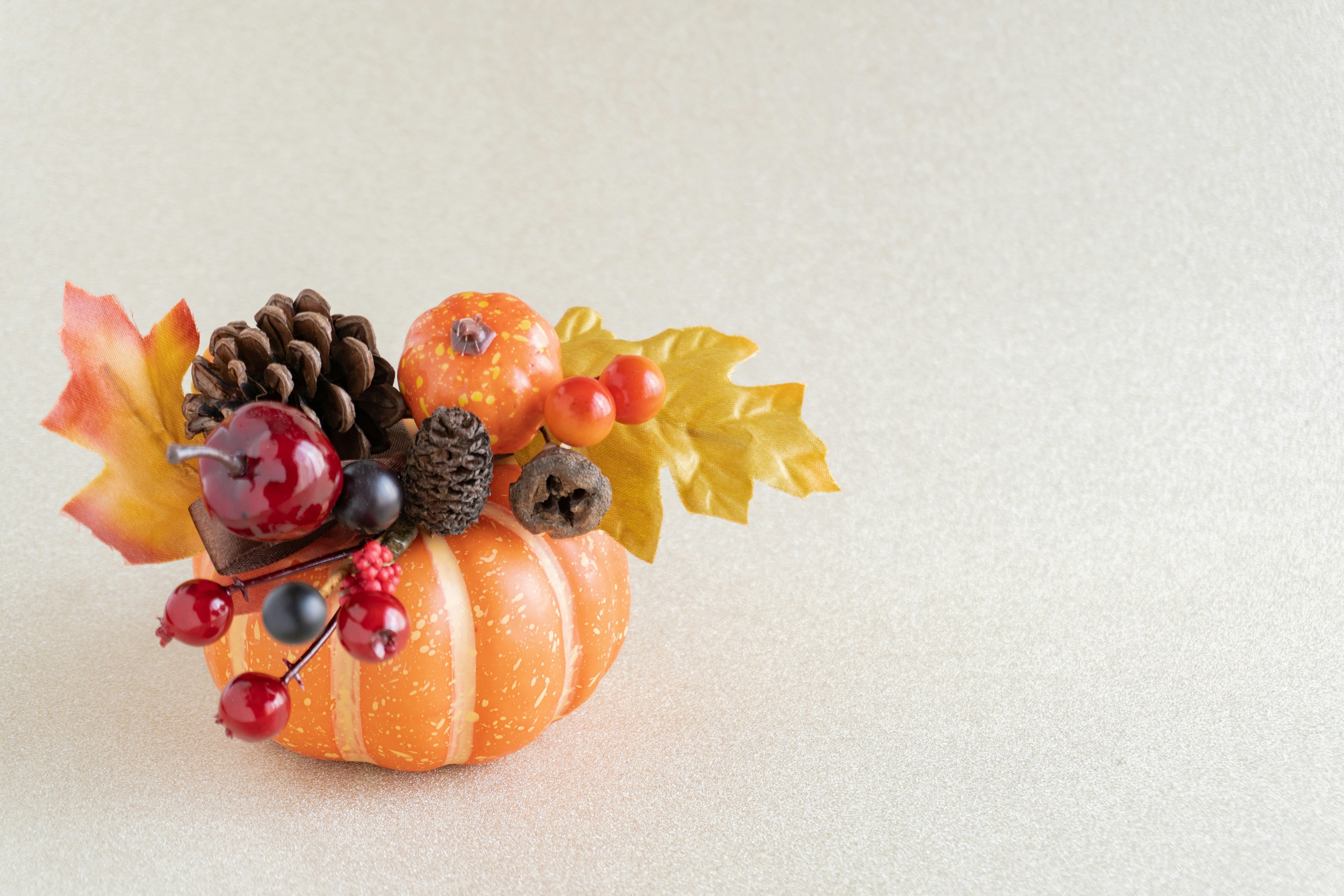 Pequeña calabaza naranja decorada con piñas y hojas coloridas