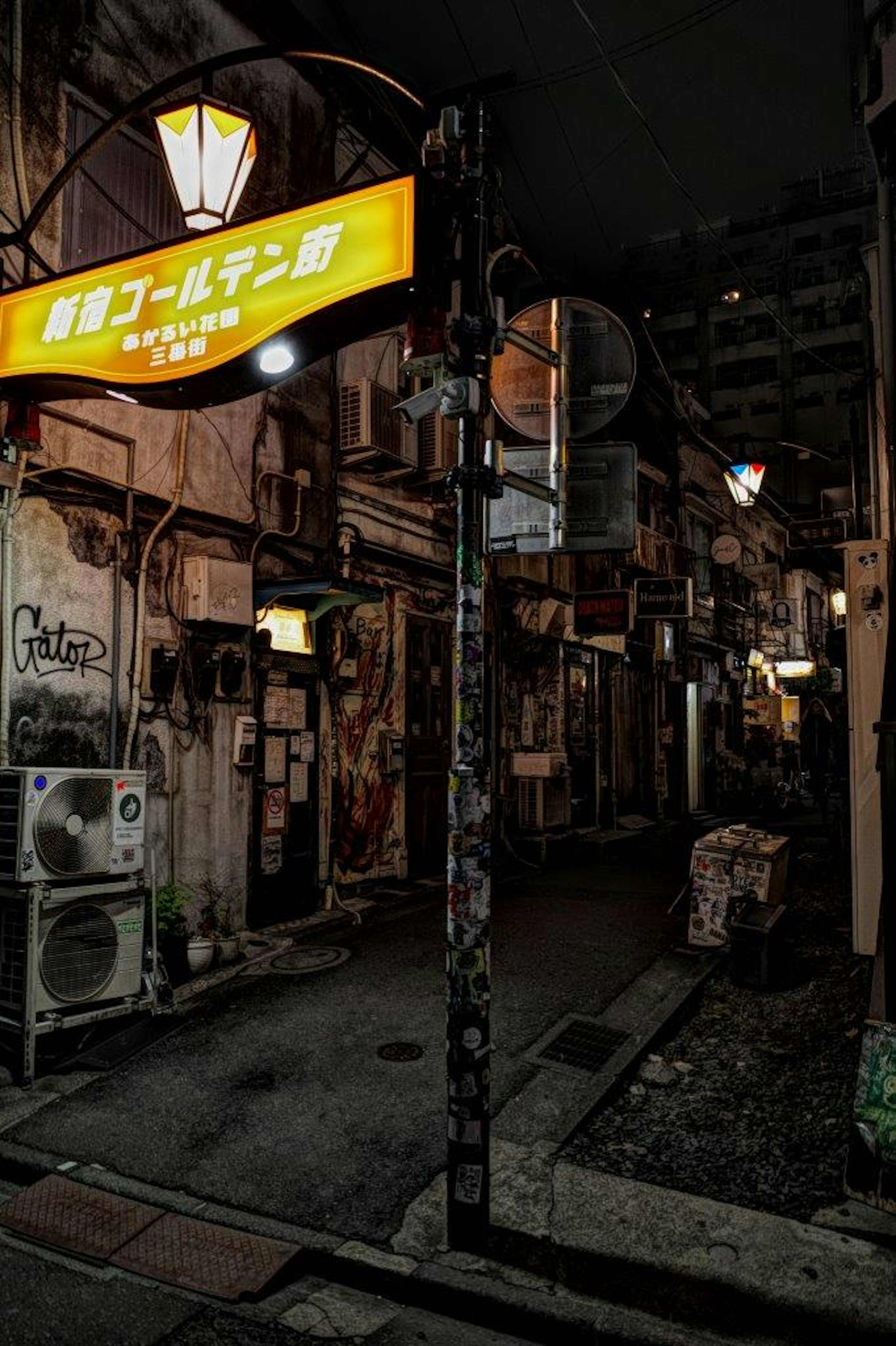 A narrow alleyway at night featuring a yellow sign and old buildings