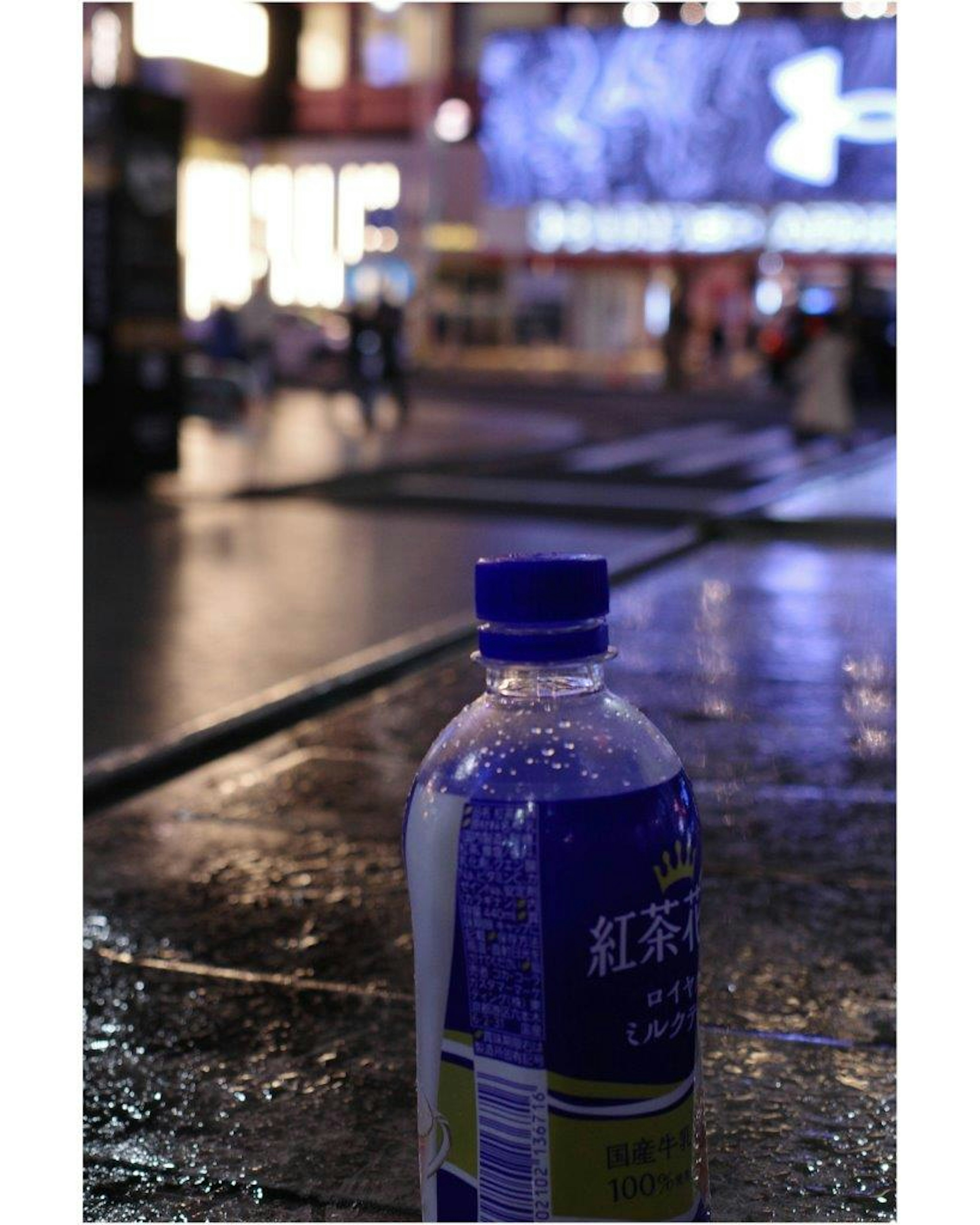 Eine blaue Getränkeflasche auf einer nassen Straße bei Nacht