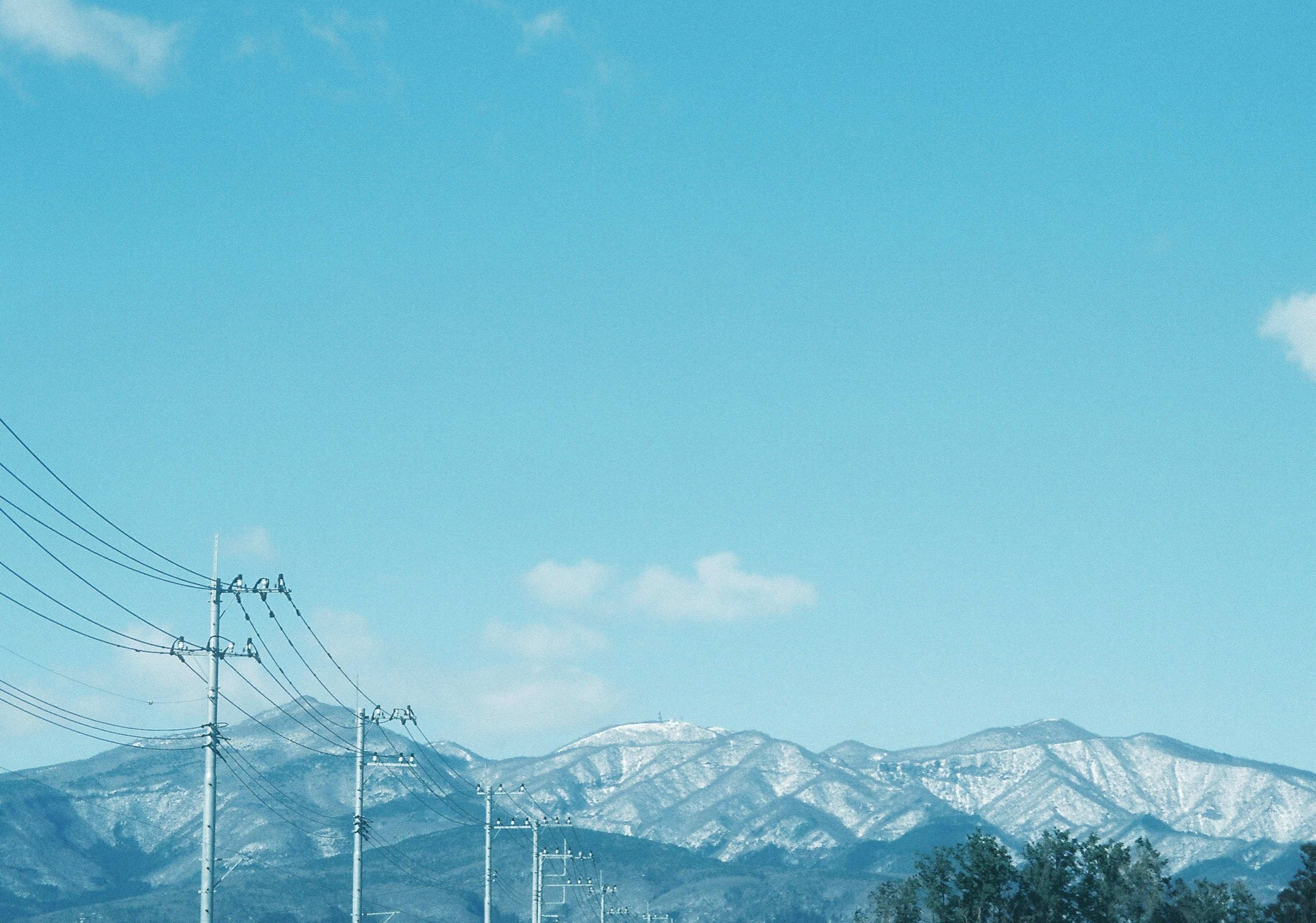 青空の下に雪をかぶった山々と電柱が並ぶ風景