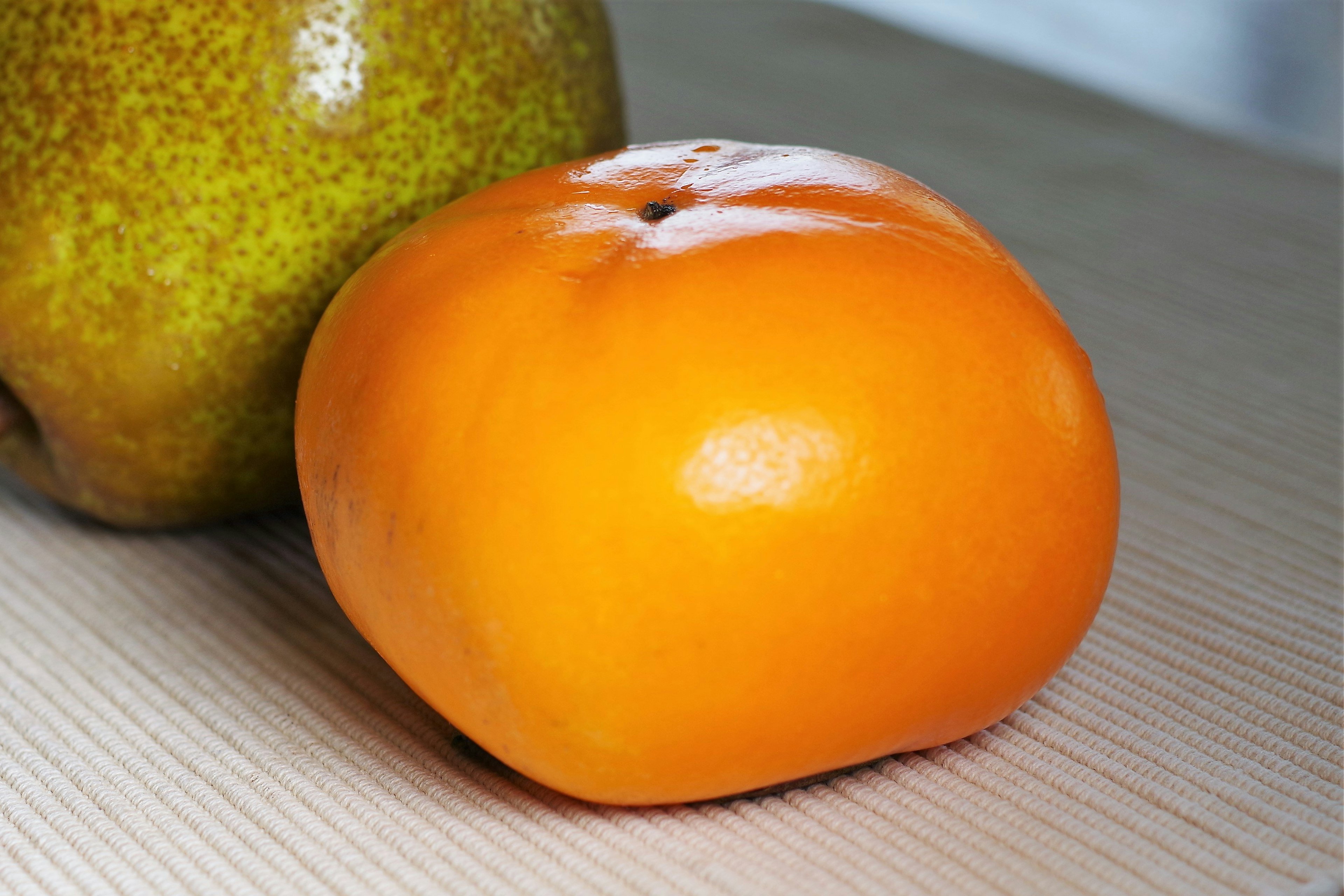 Image montrant un kaki orange à côté d'une poire verte