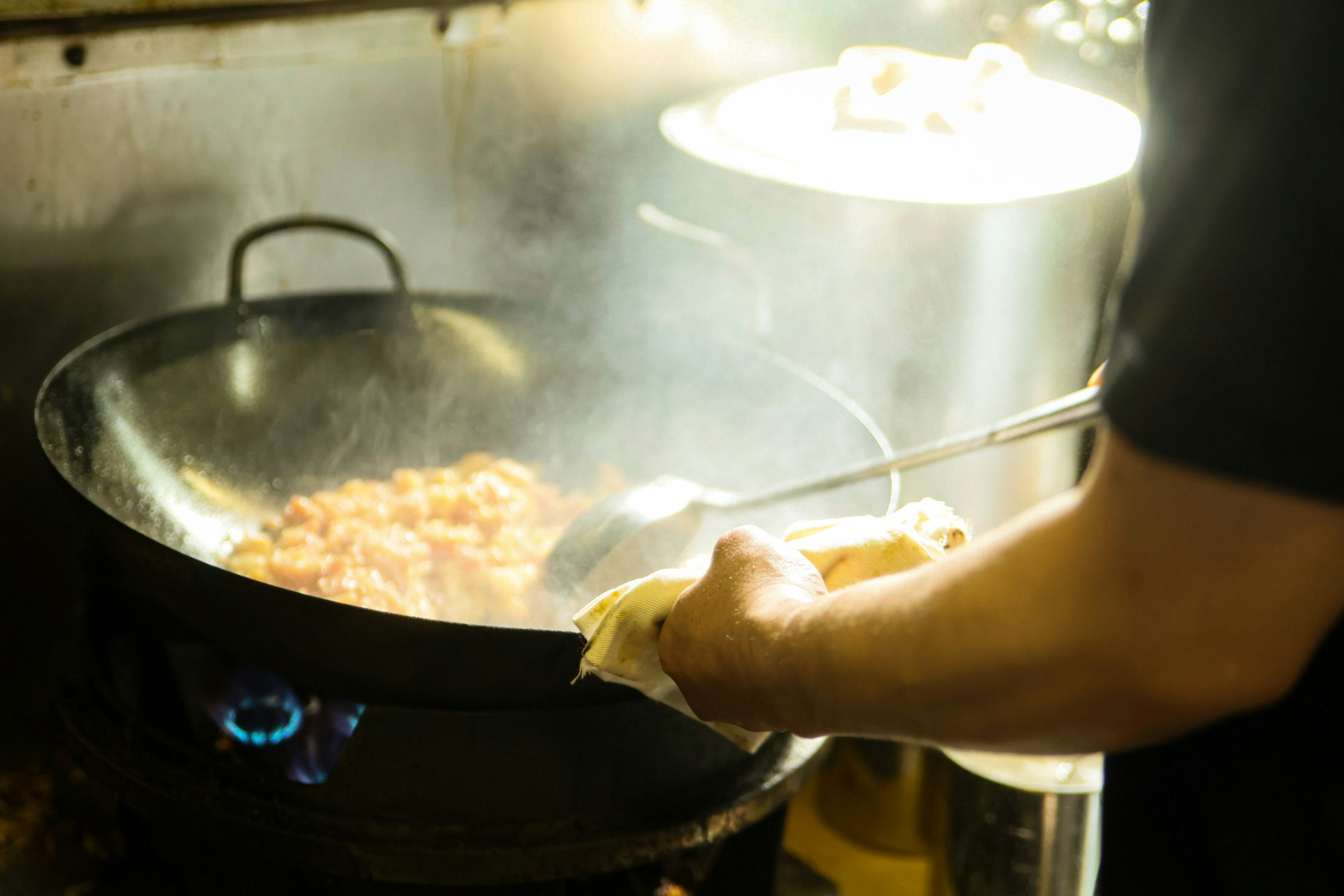 Scène de cuisson avec un wok et une main remuant de la nourriture vapeur qui monte