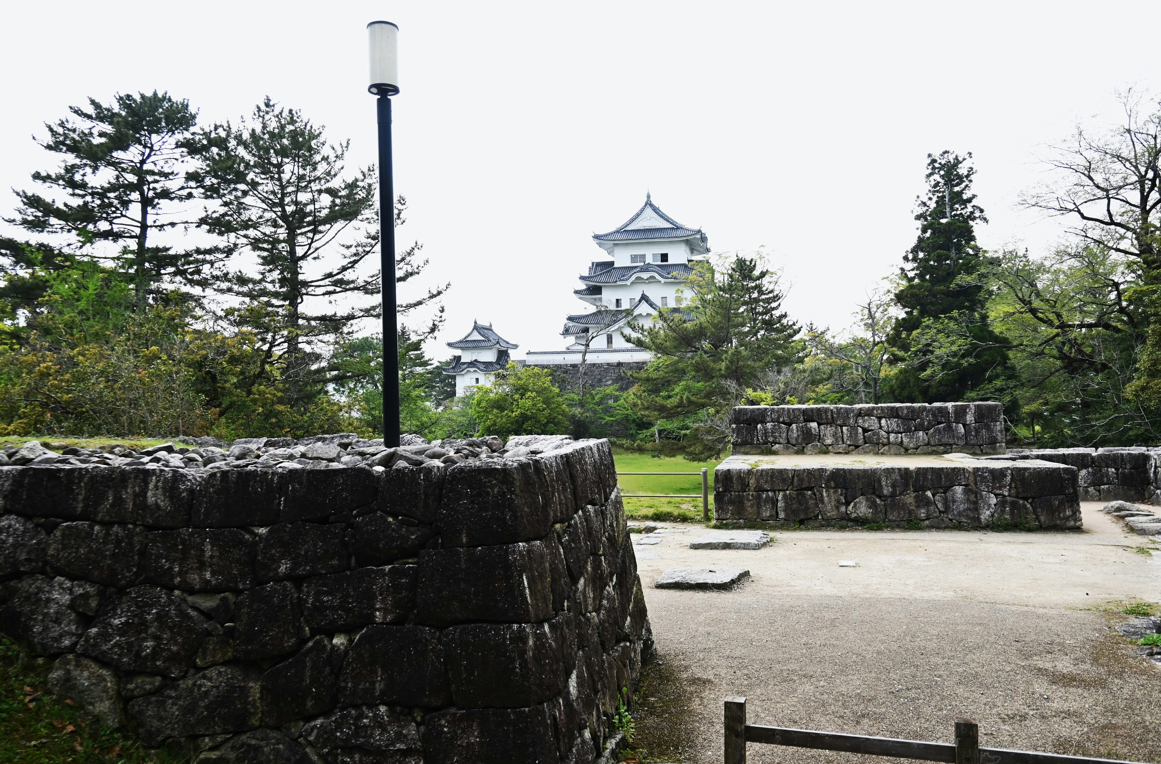 Vista panoramica con muri di pietra e un castello sullo sfondo circondato da vegetazione