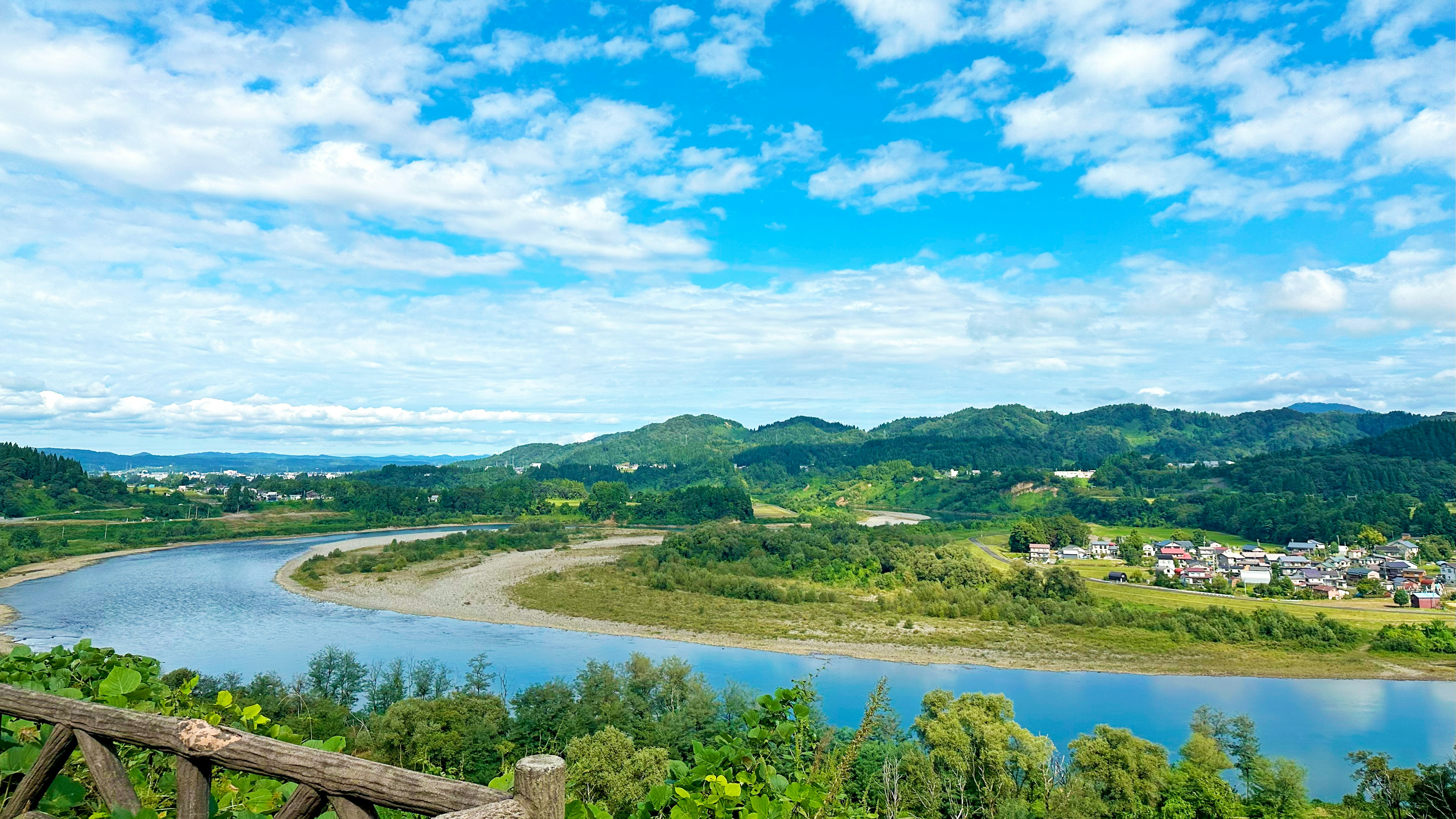 Scenic view of a river flowing through lush green hills under a bright blue sky