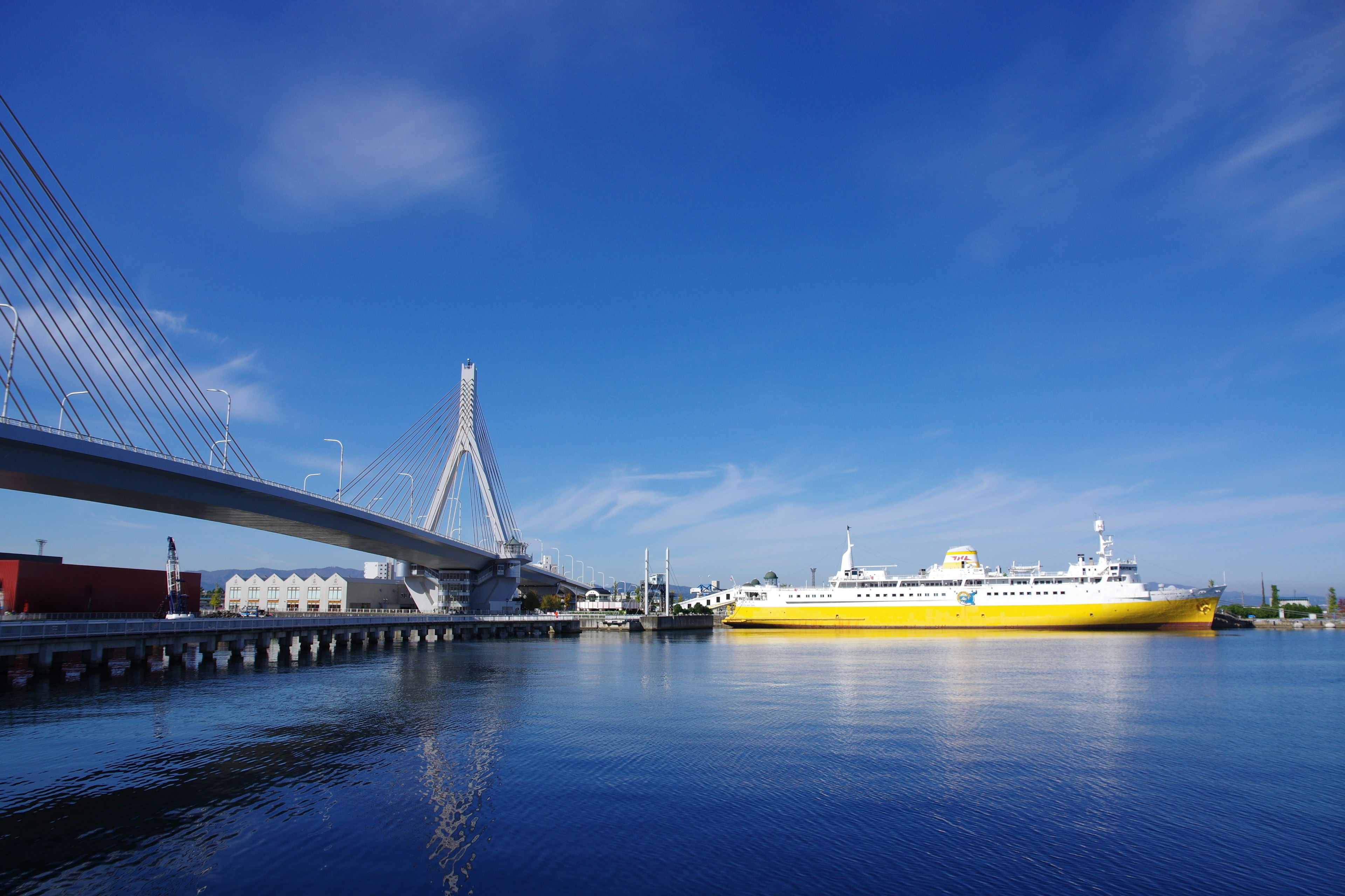 Scène portuaire avec un bateau jaune et un pont moderne sous un ciel bleu