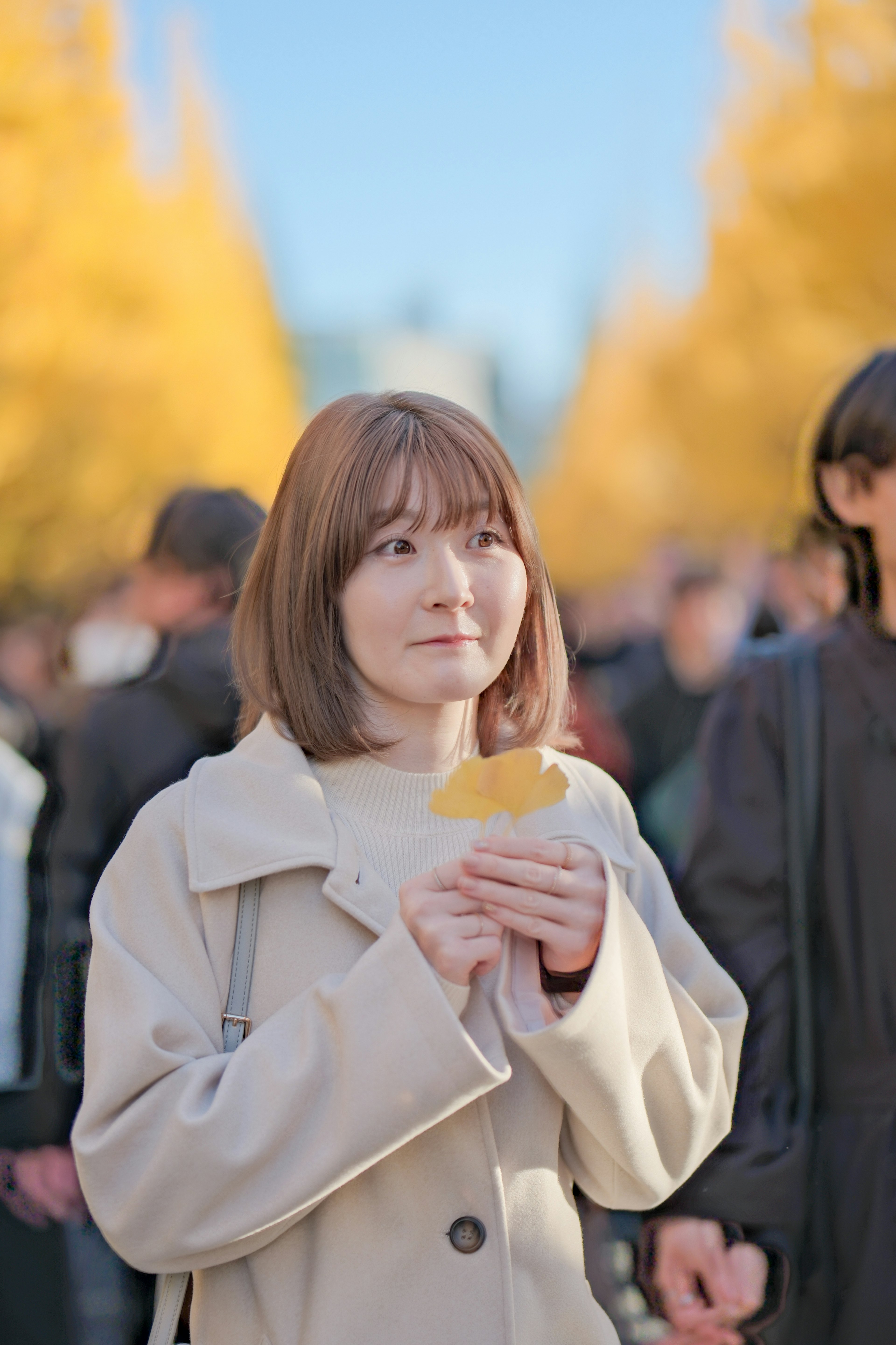 Una donna che tiene una foglia gialla si trova tra la folla in un parco autunnale