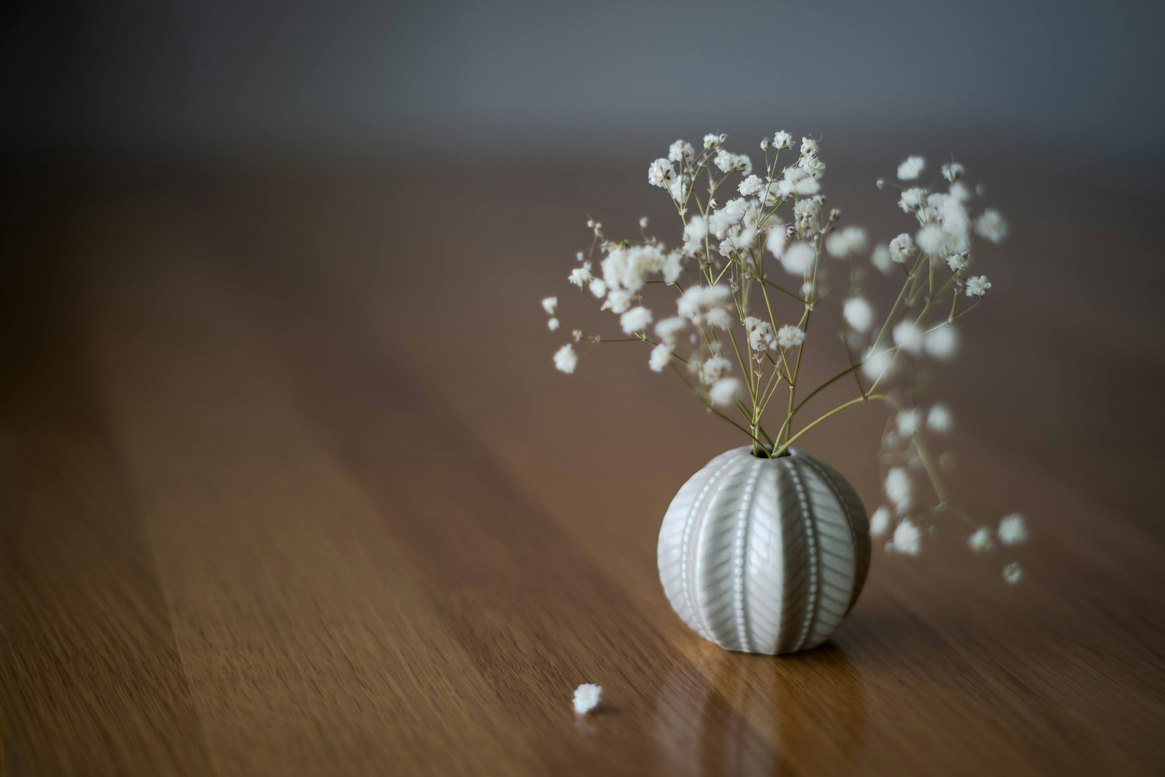 A round vase with white flowers placed on a wooden table in a simple arrangement