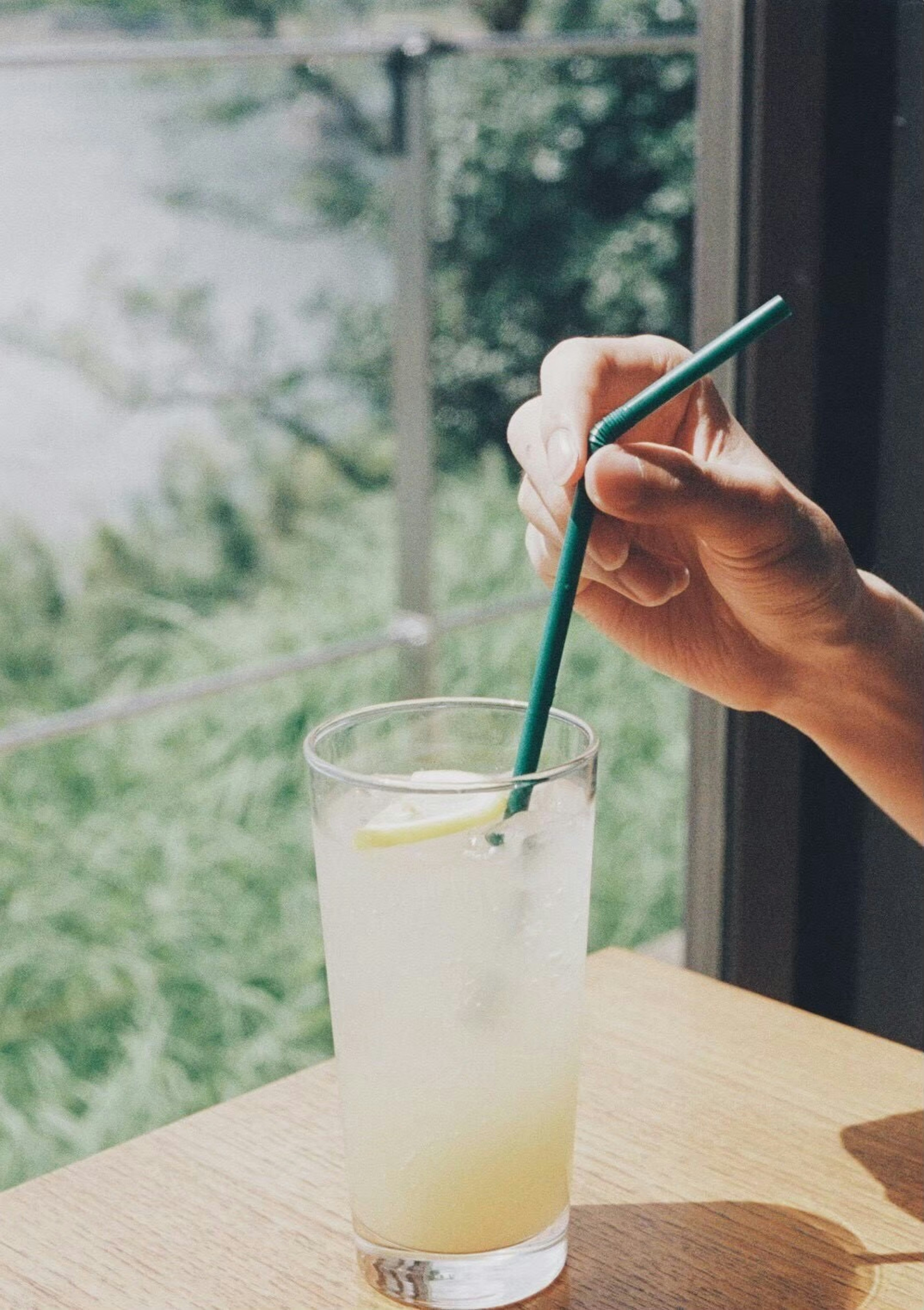 Eine Hand hält einen grünen Strohhalm in einem Glas Limonade mit einer Zitronenscheibe