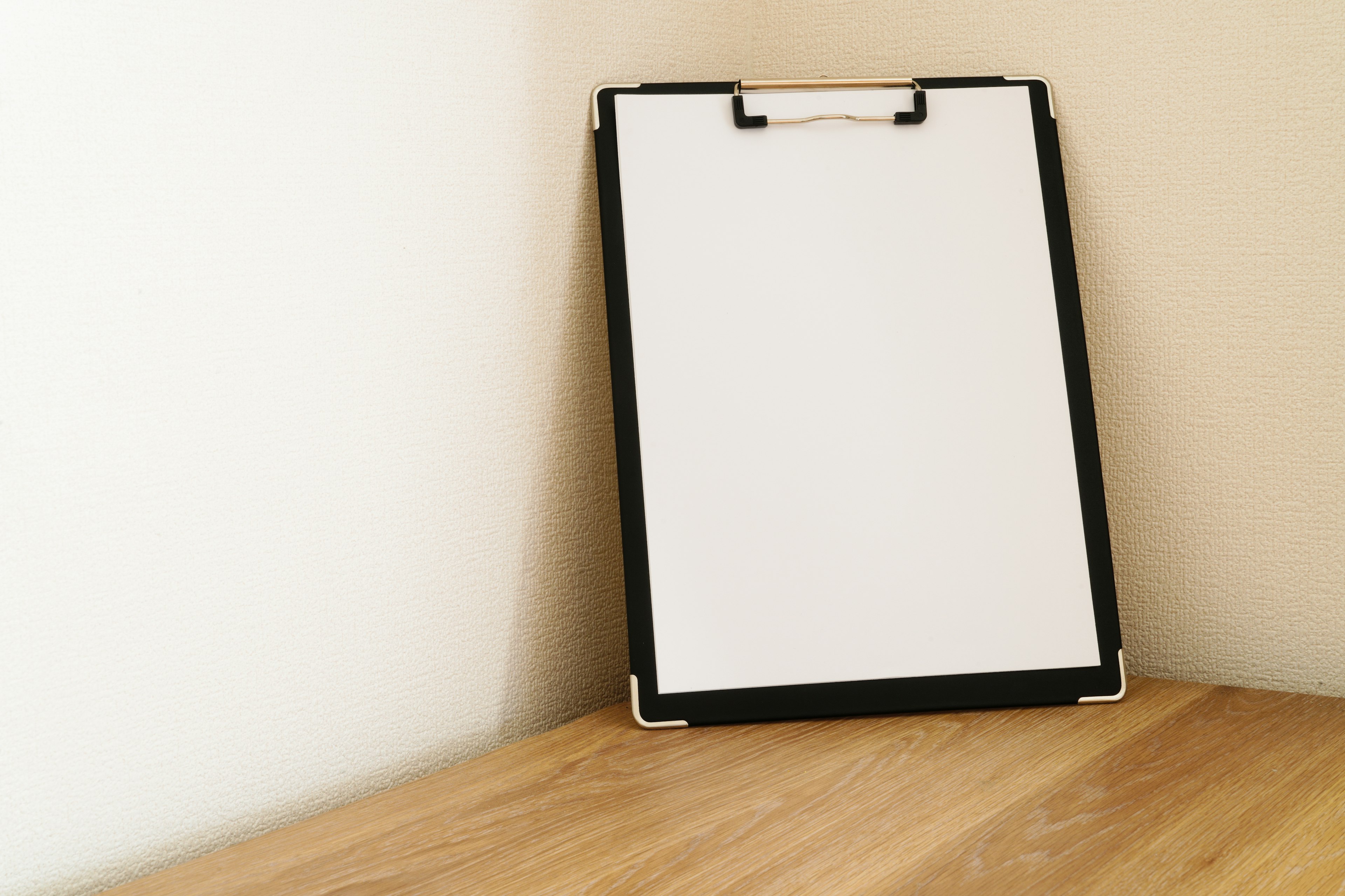 A white clipboard positioned in the corner of a wooden table