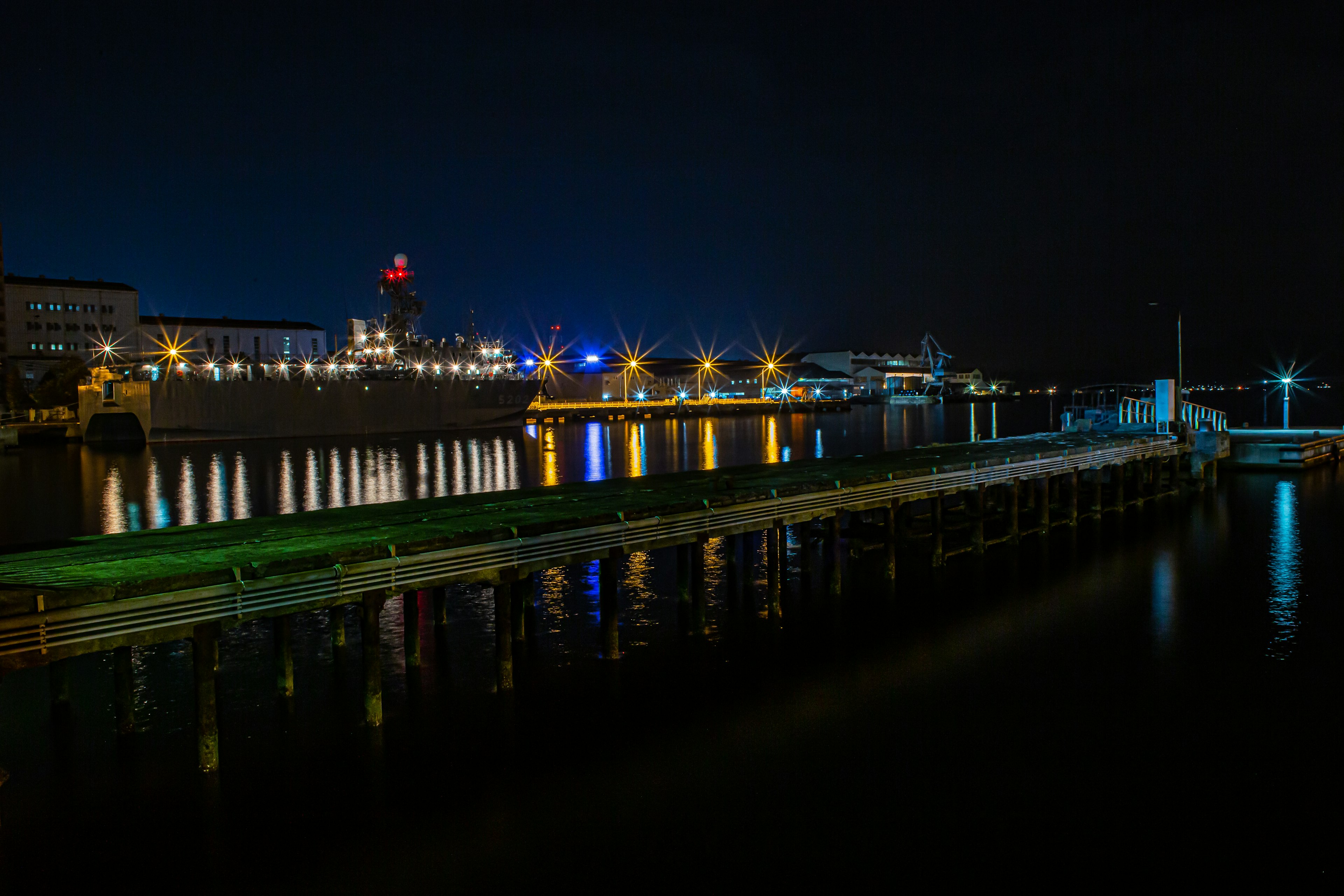 Vista notturna di un porto con luci che si riflettono sull'acqua e un ponte