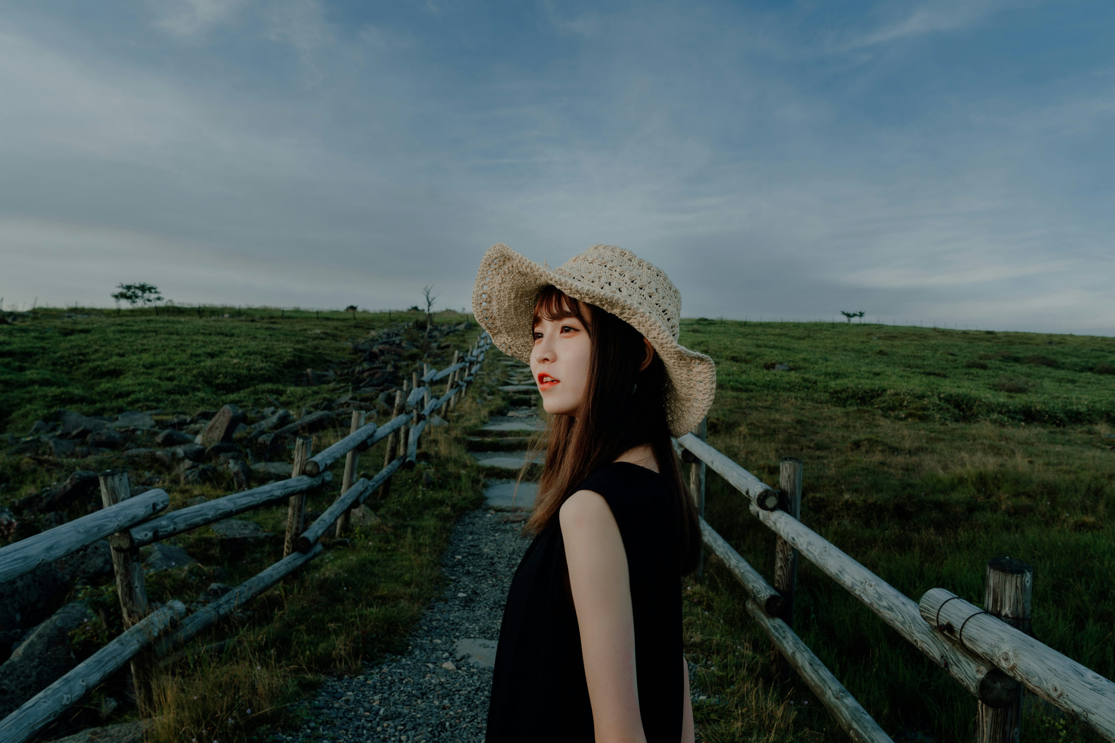 Mujer caminando por un sendero verde con un sombrero de paja y vestido negro