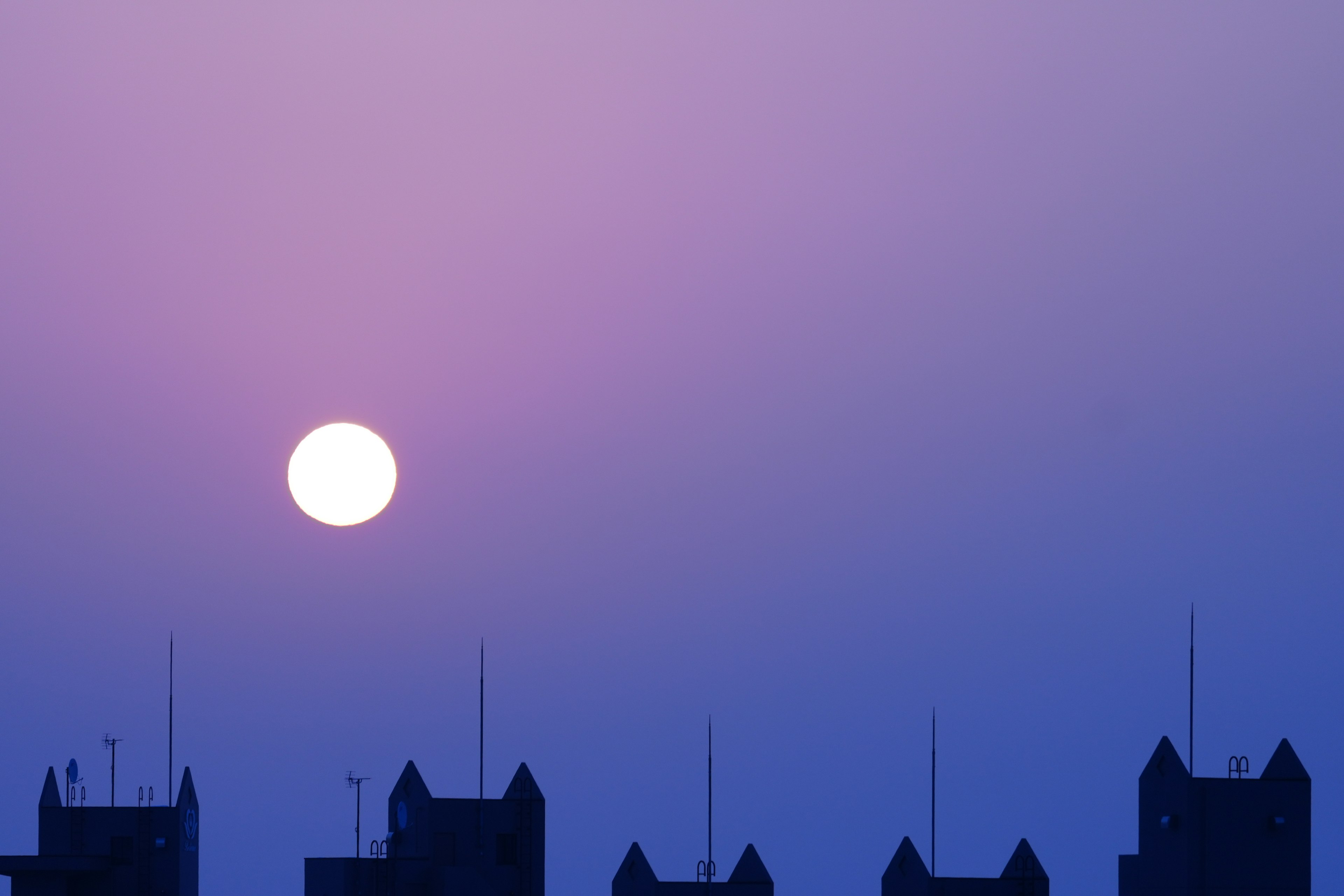 Grand soleil se couchant dans un ciel violet avec silhouettes de bâtiments