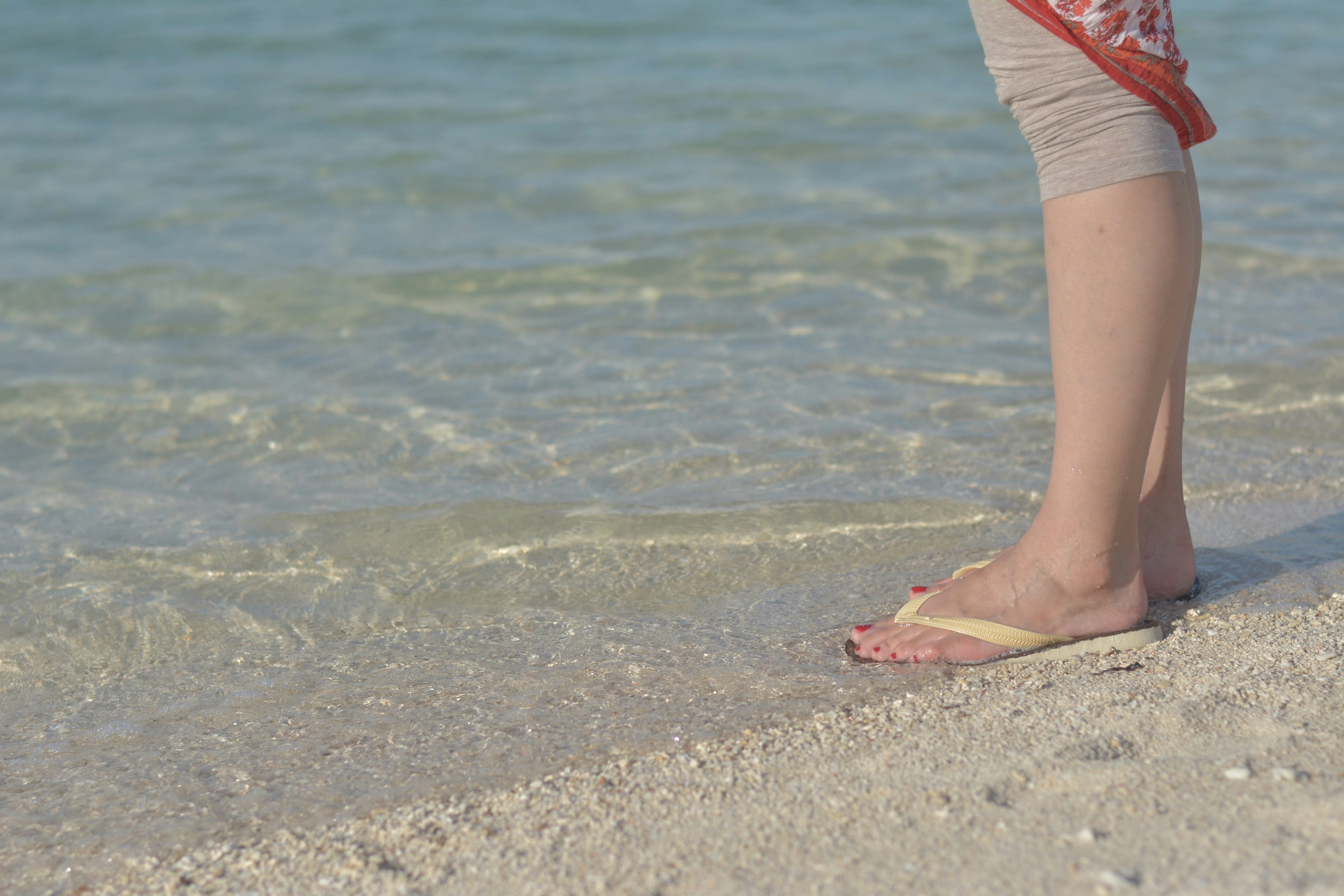 Close-up of feet standing by the sea wearing sandals