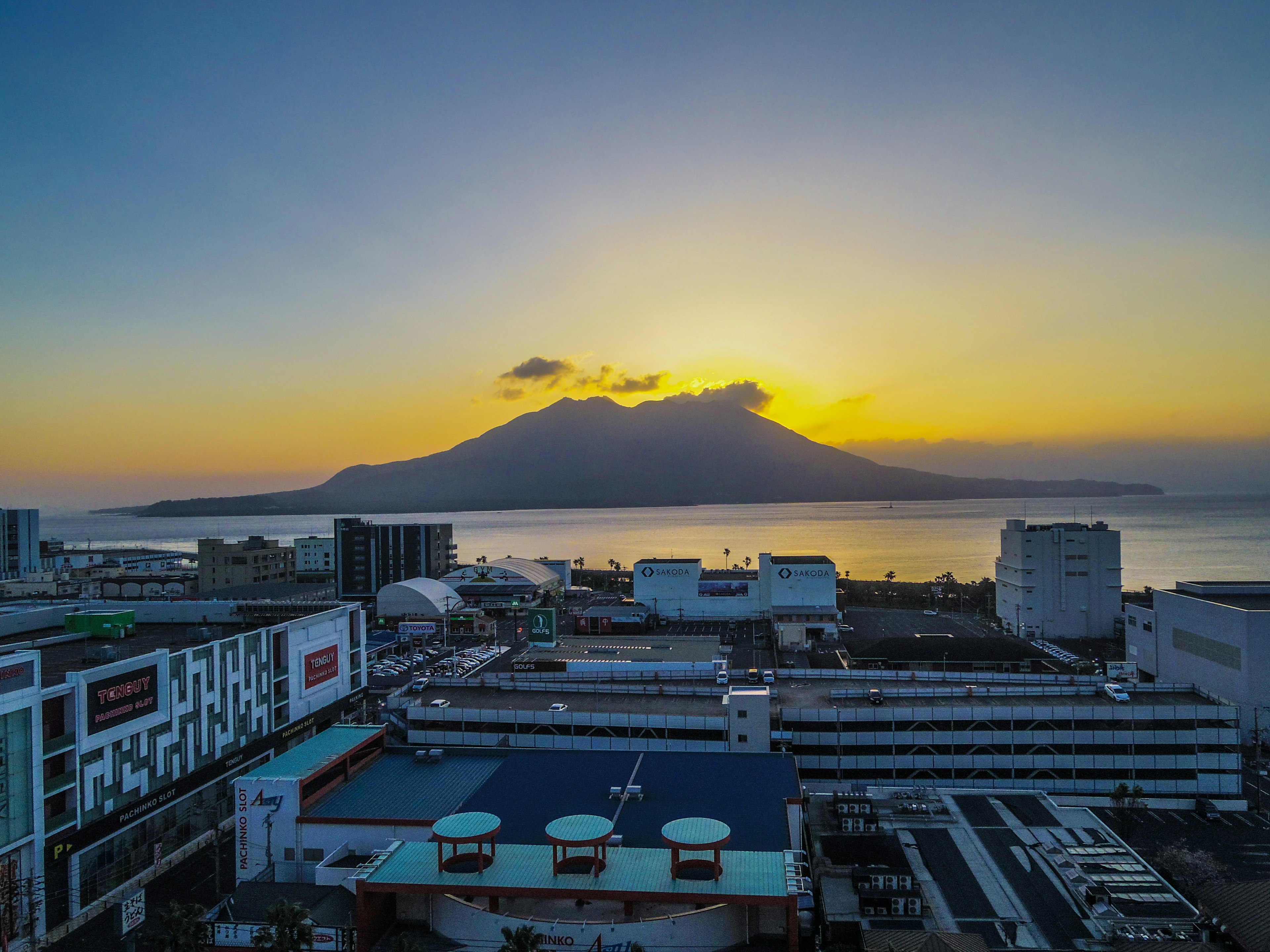 夕日を背景にした山と海の壮大な景色 近くの建物と商業施設が見える