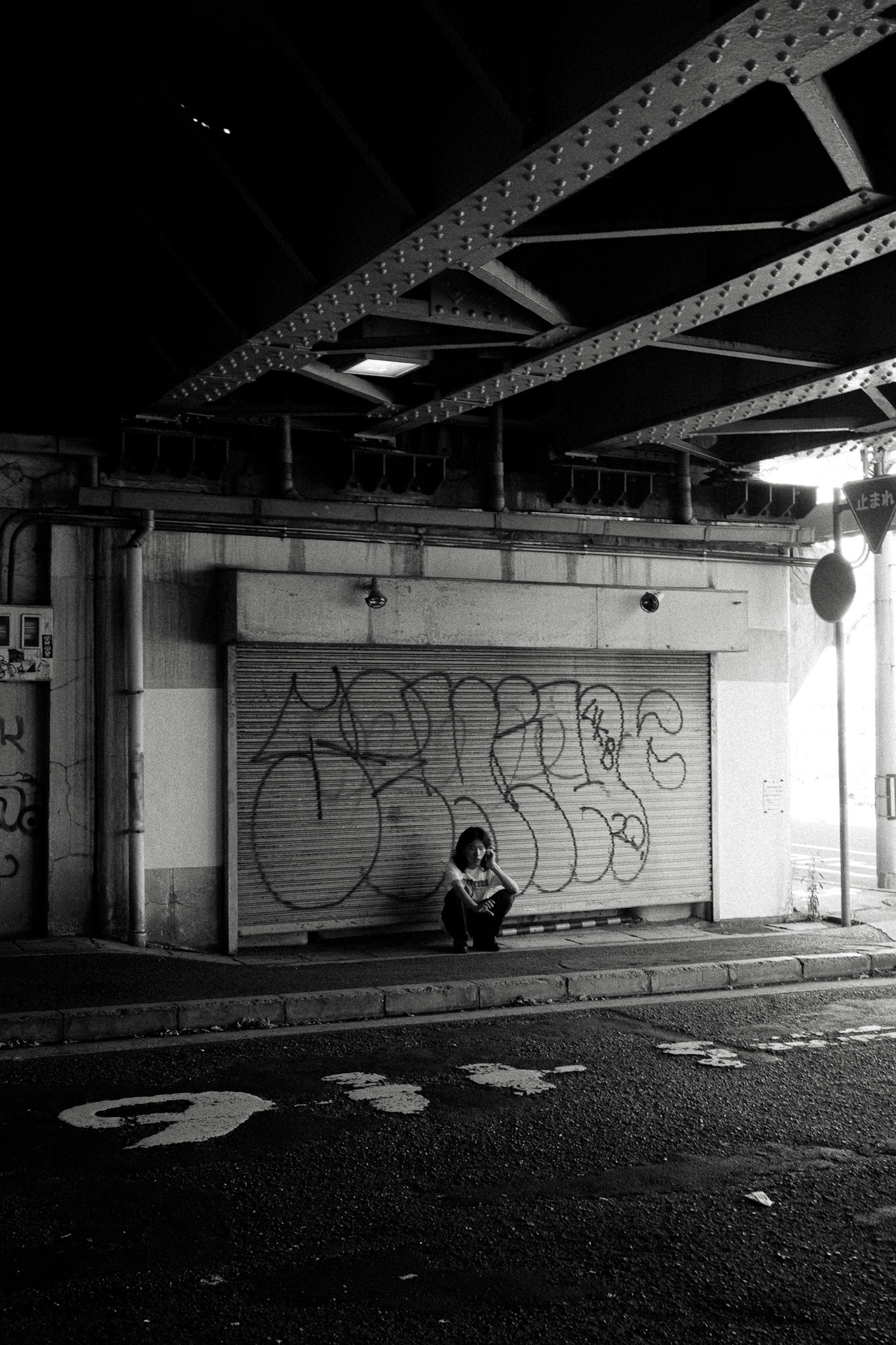 Une personne assise sous un pont avec des graffitis sur le mur