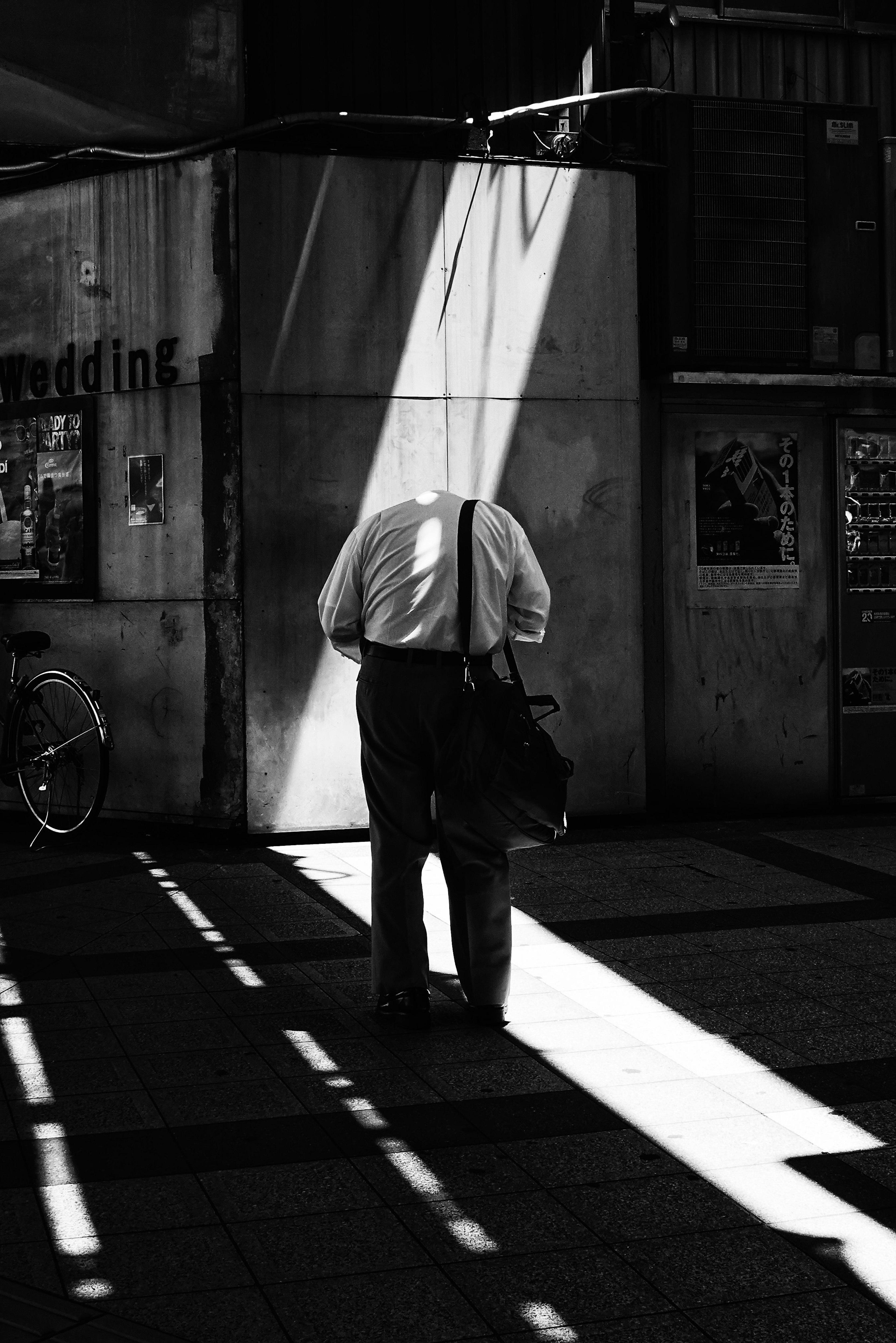 白黒の街角で背を向けて歩く男性の姿 光のストライプが地面に落ちている