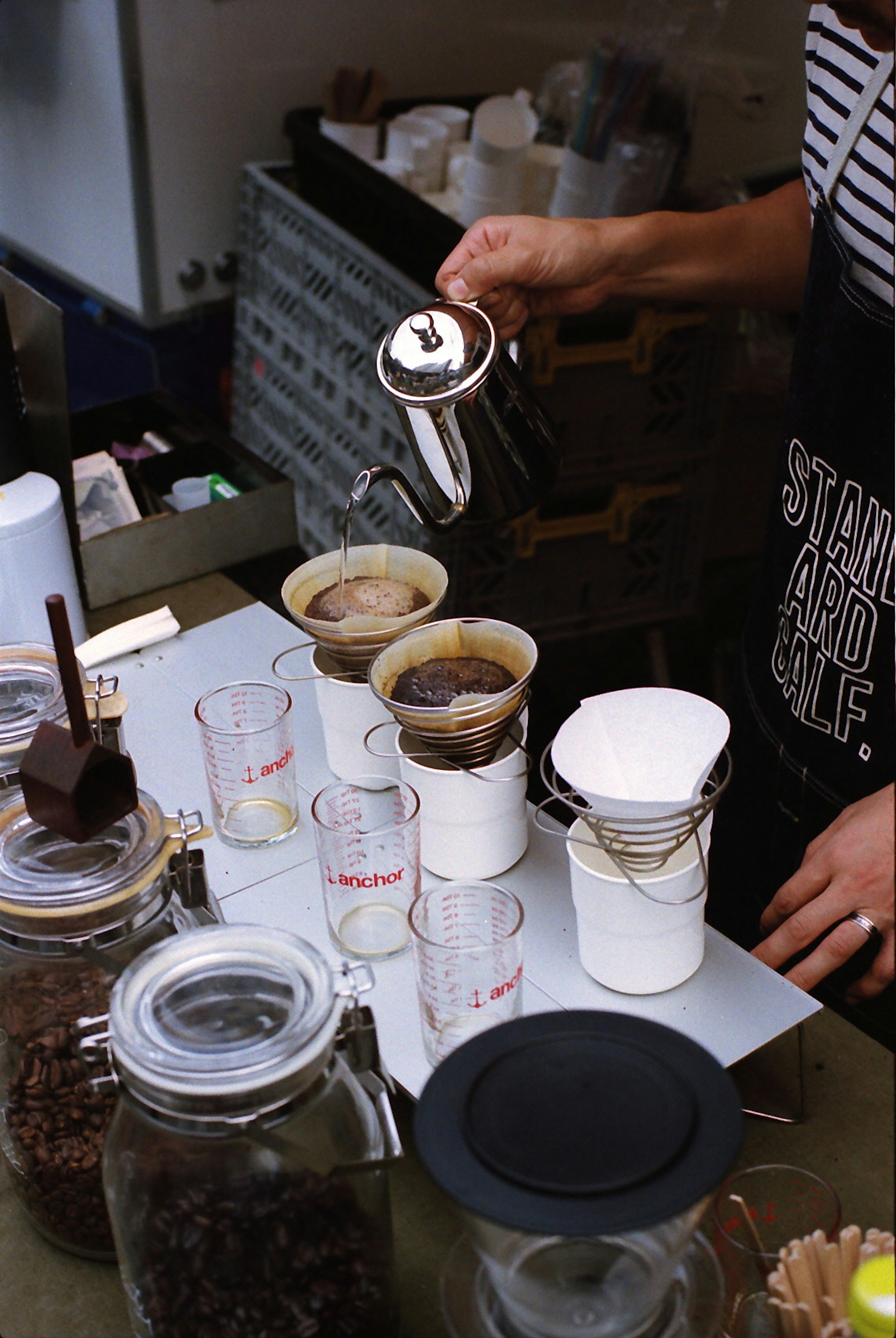 Un barista vertiendo café en dispositivos de preparación con frascos de vidrio y café molido