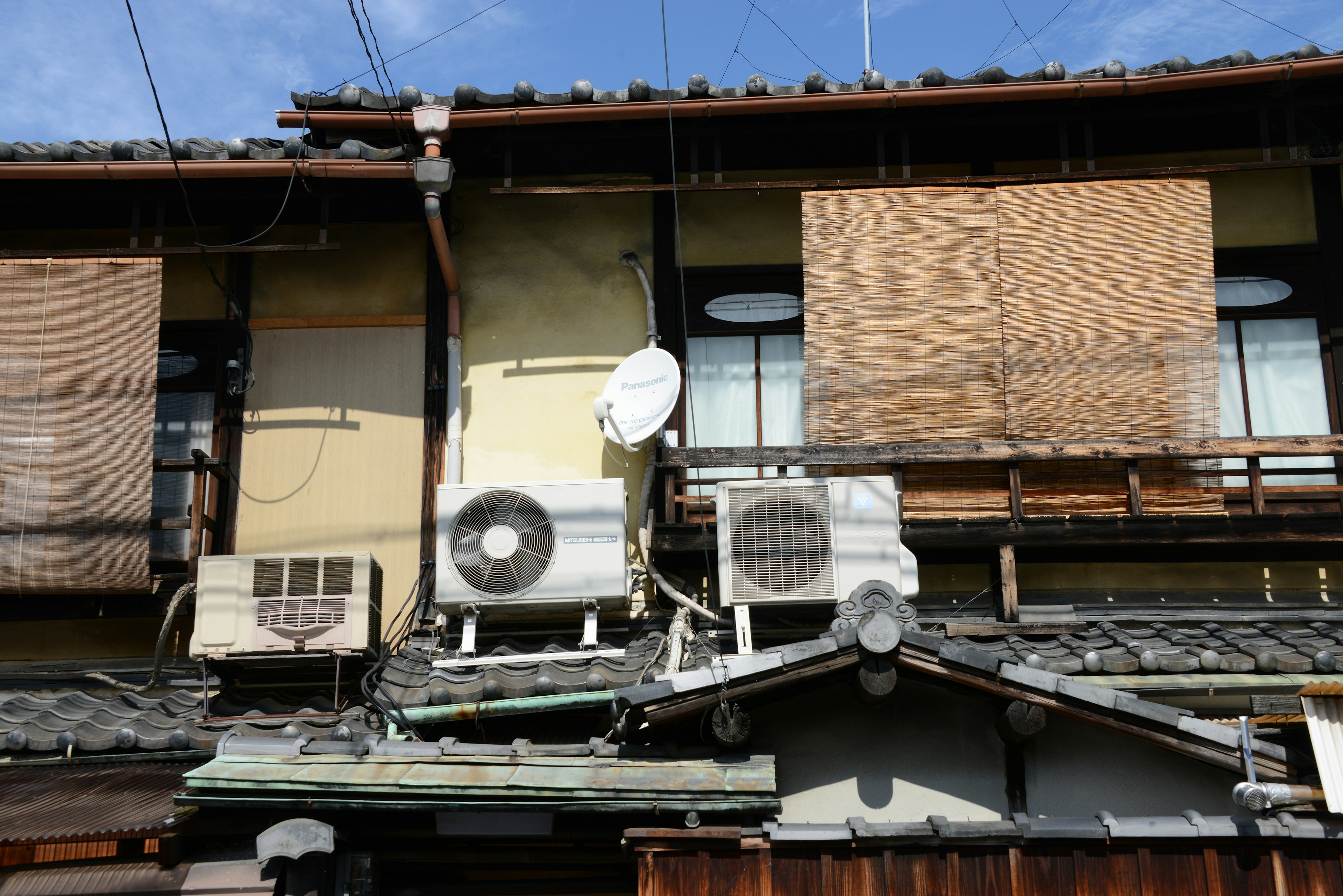 Exterior de una vieja casa japonesa con persianas de bambú unidades de aire acondicionado y una antena satelital