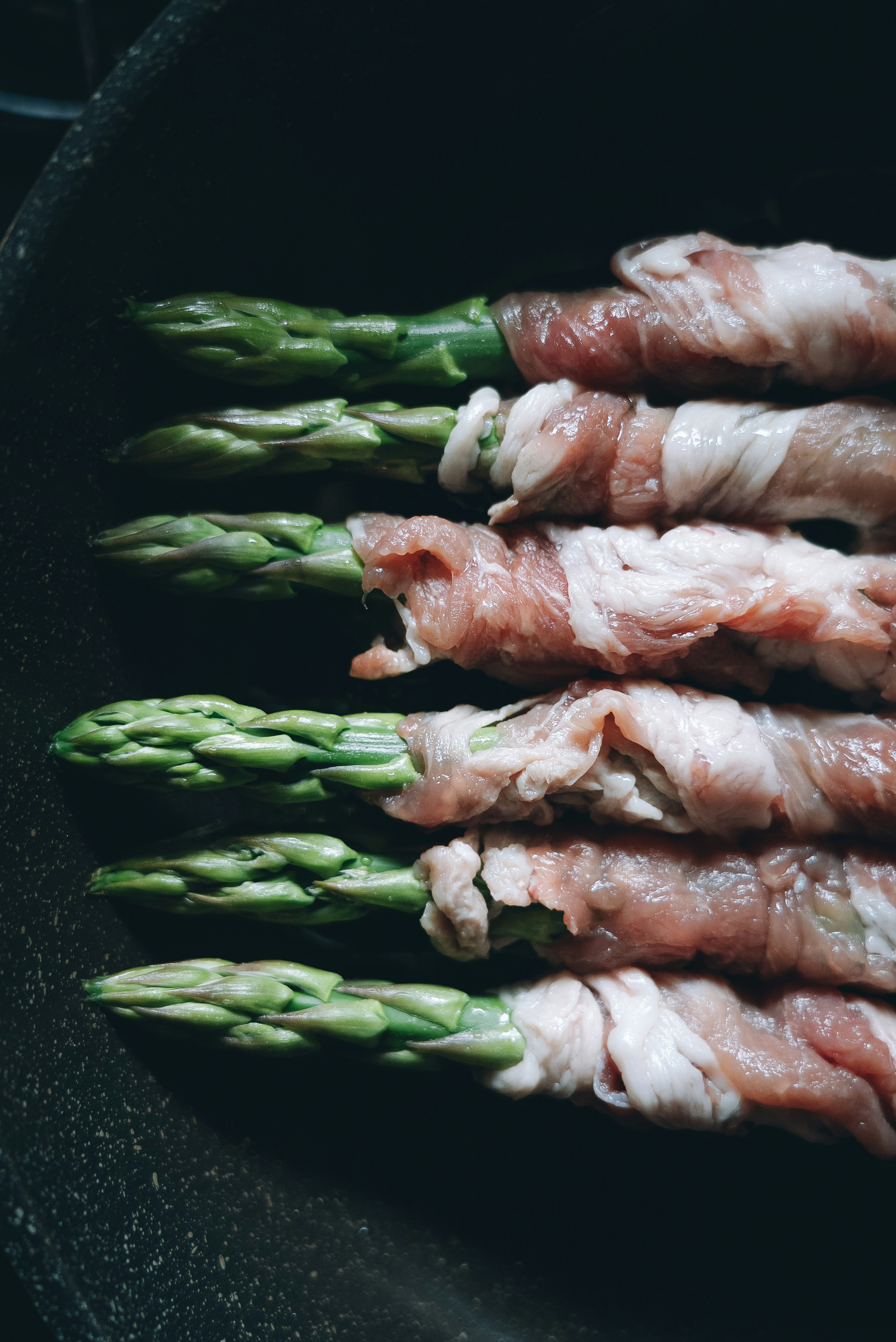 Asparagus wrapped in bacon arranged in a pan