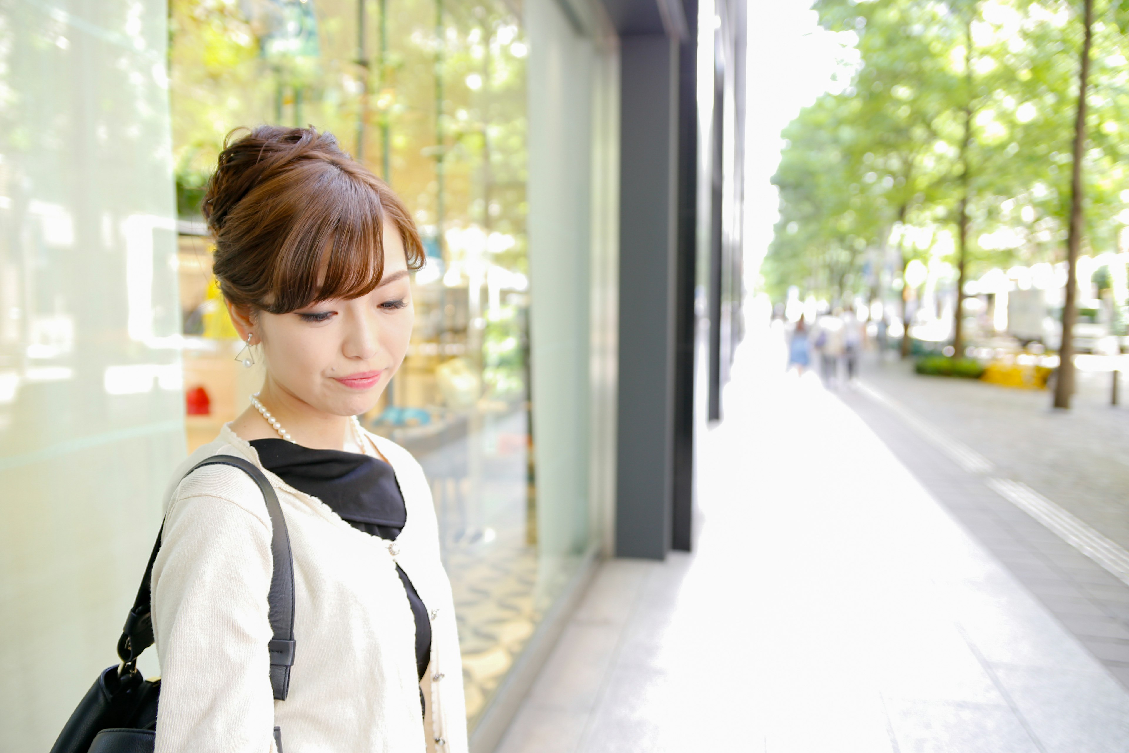 A woman pondering on a city street with green trees and bright sunlight in the background