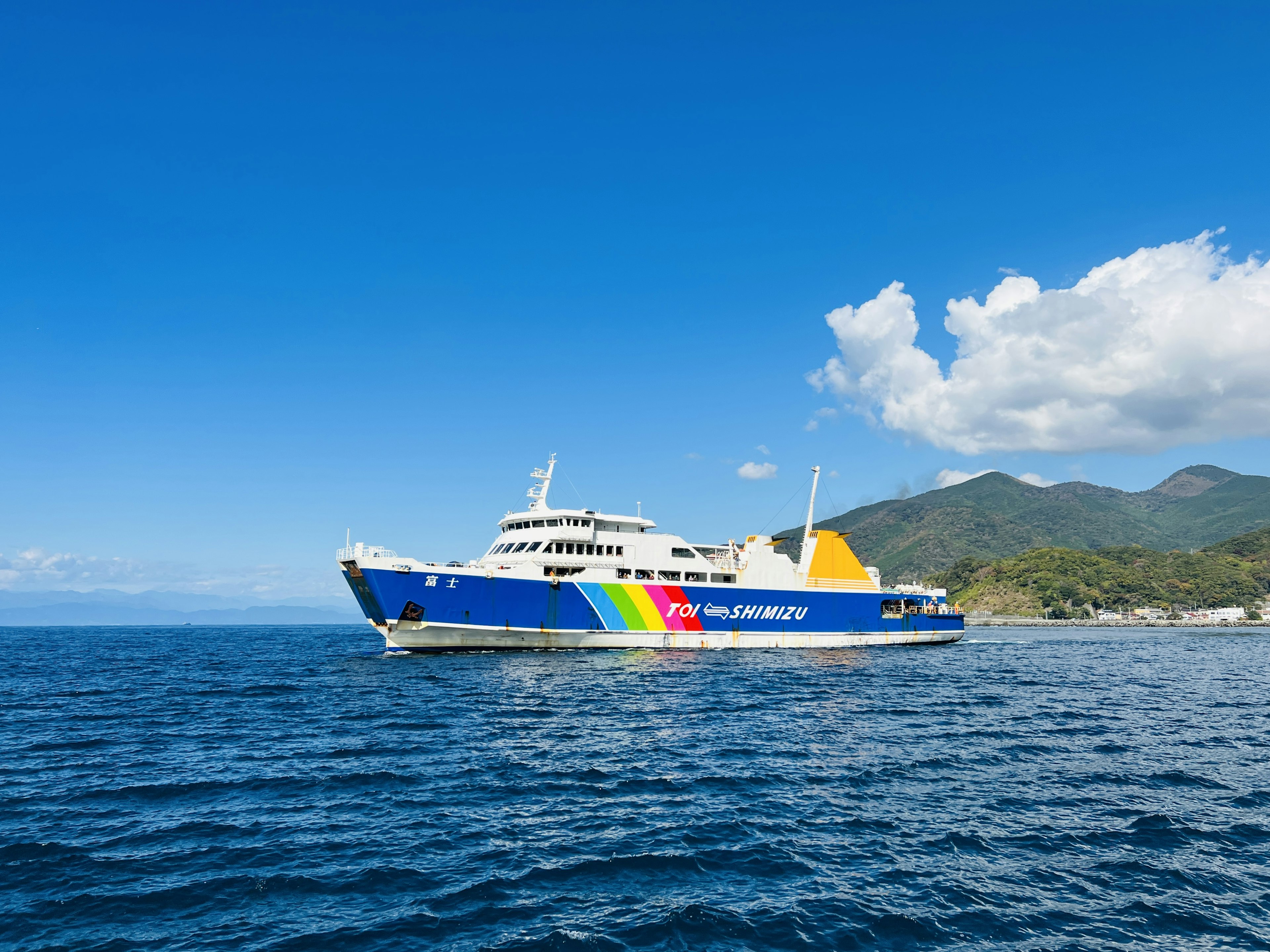 Ferry berwarna-warni berlayar di lautan biru dengan gunung di latar belakang