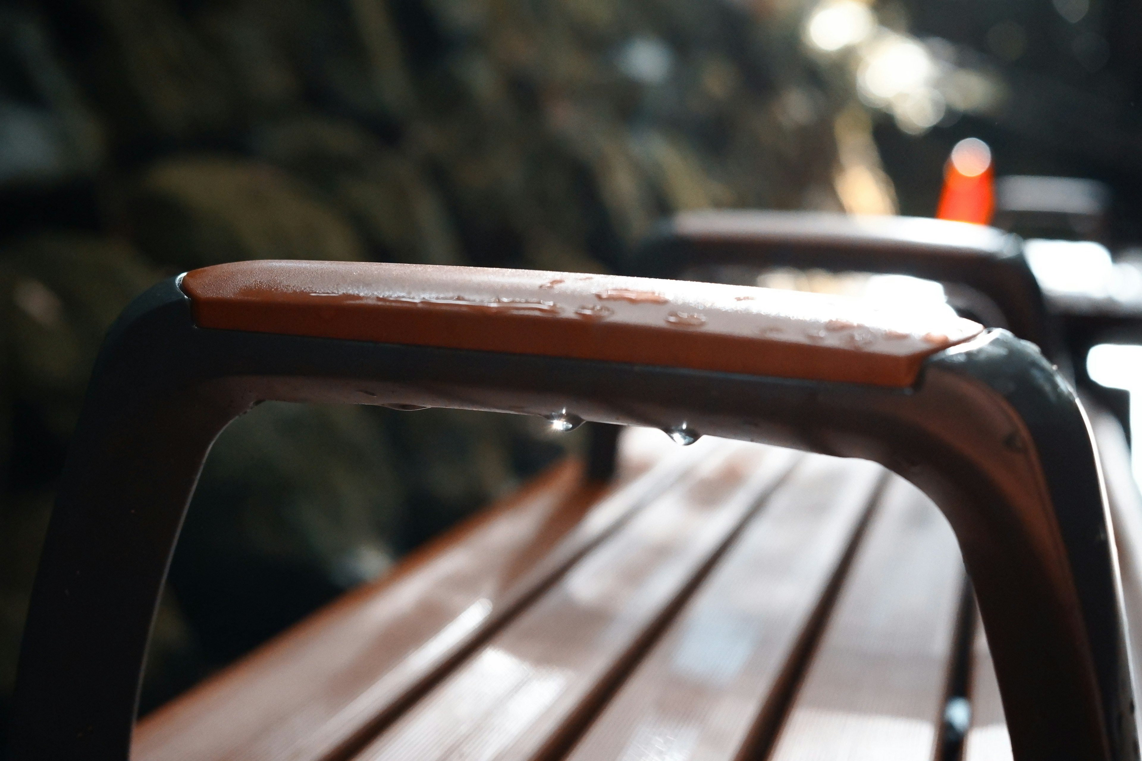 Close-up of a wet metal handle and wooden bench