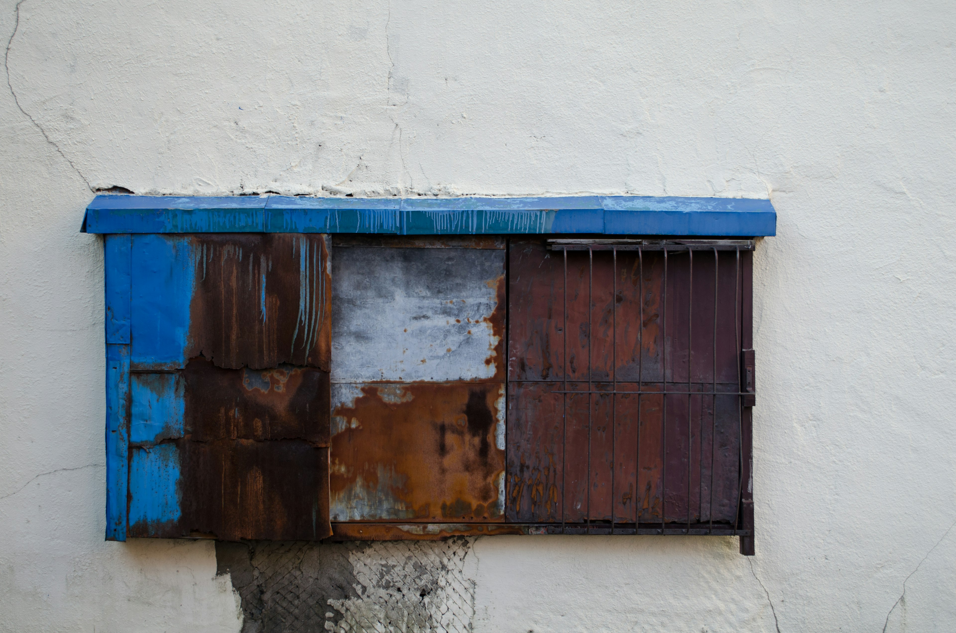 Altes Holzfenster mit blauem Dach an einer weißen Wand