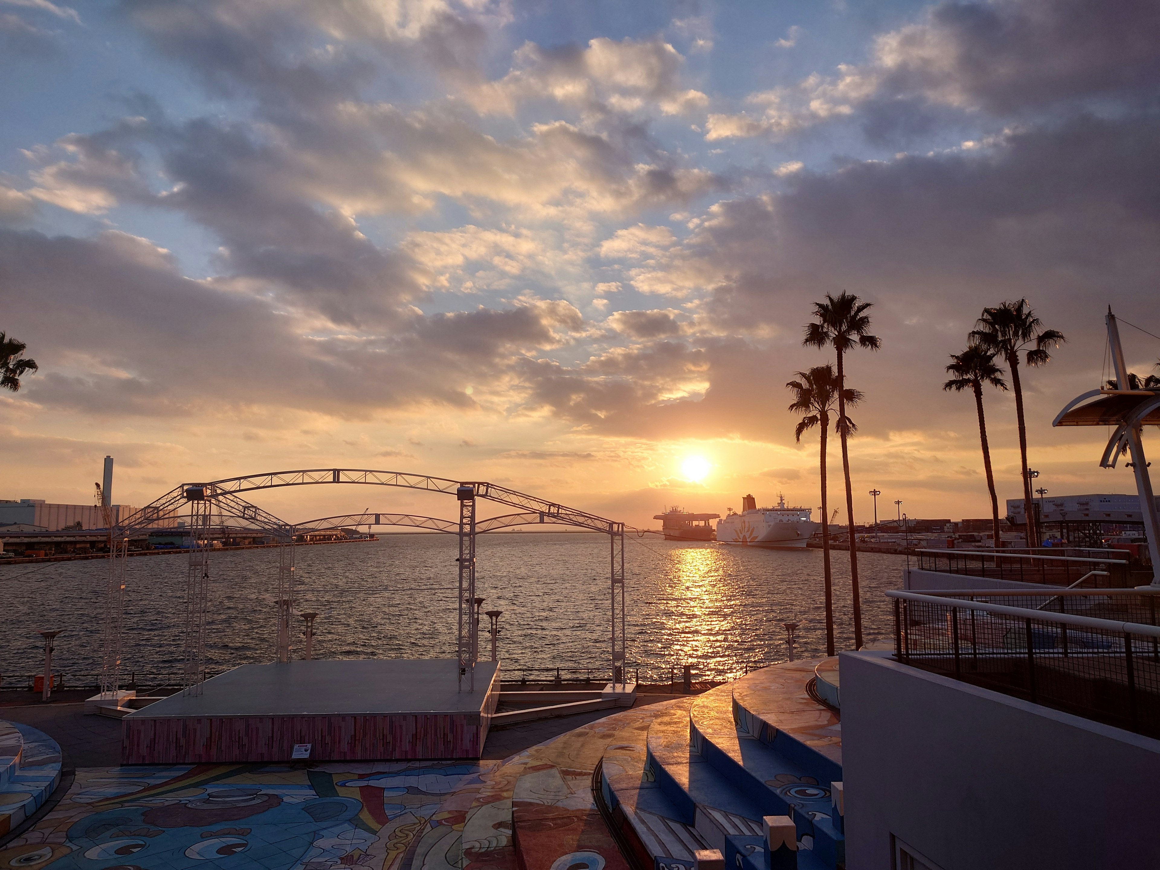 夕焼けの海岸線に立つヤシの木と船のシルエット