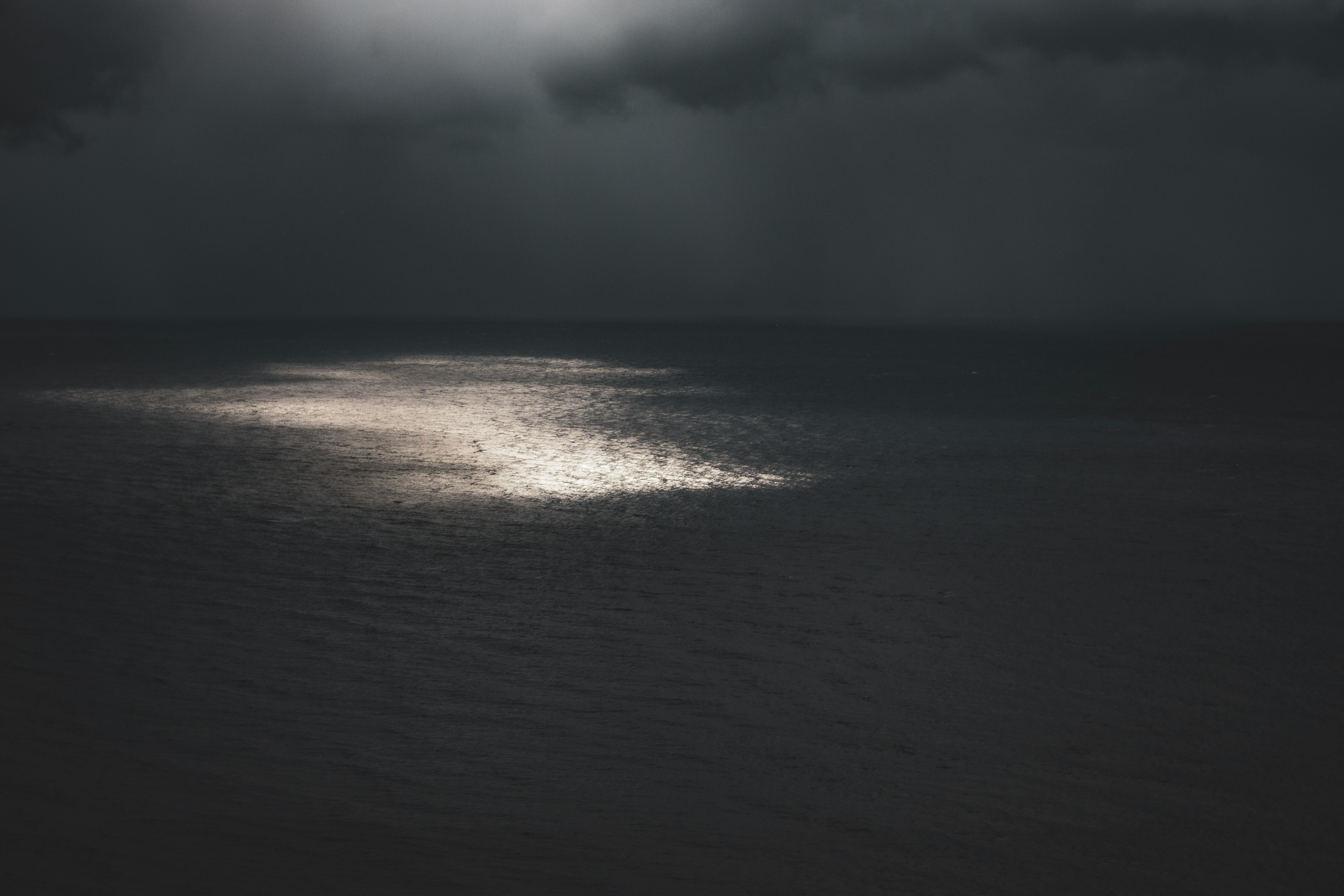 Mare scura con una striscia di luce riflessa e nuvole