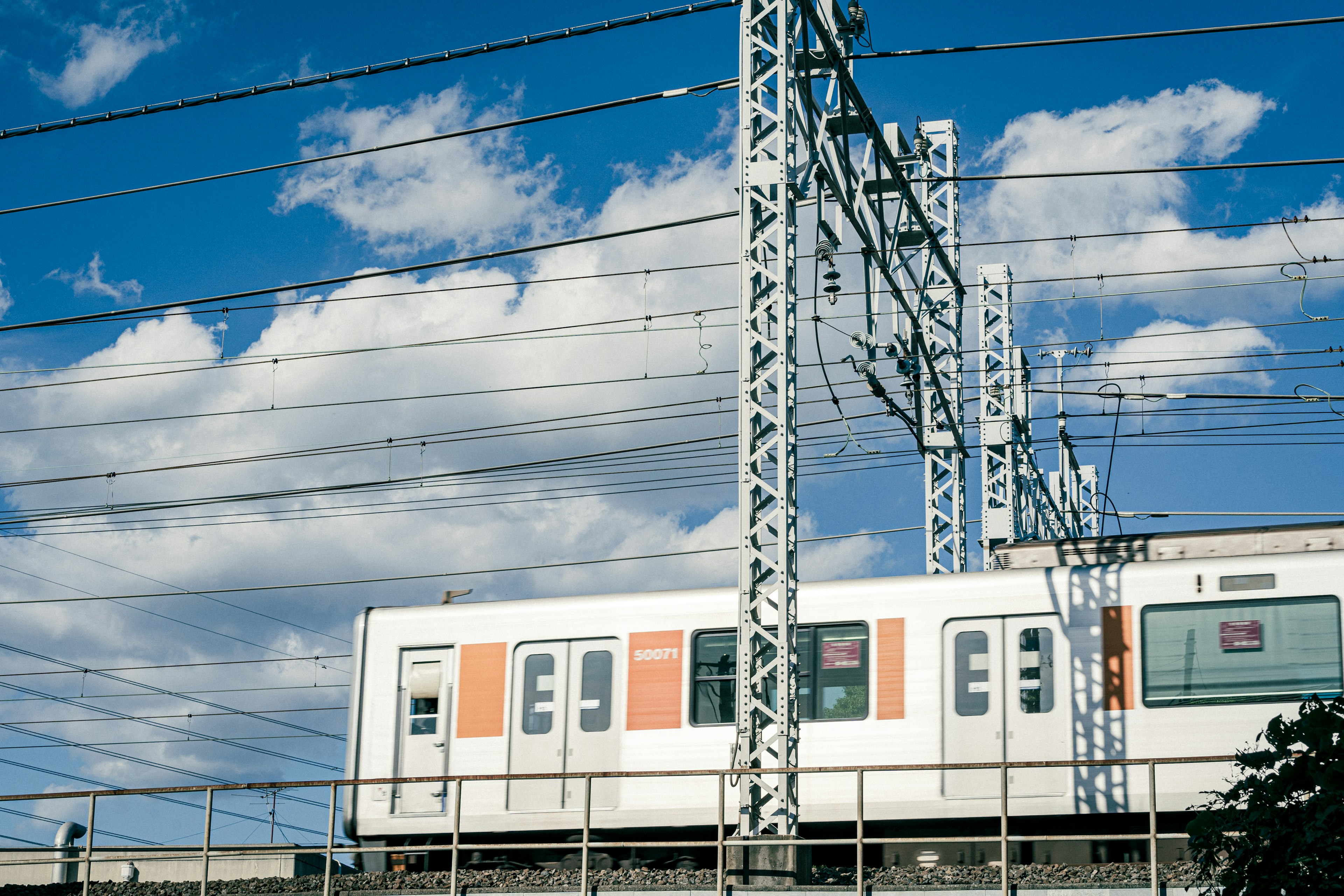 青空の下を走る電車の画像 鉄道の架線と電柱が見える