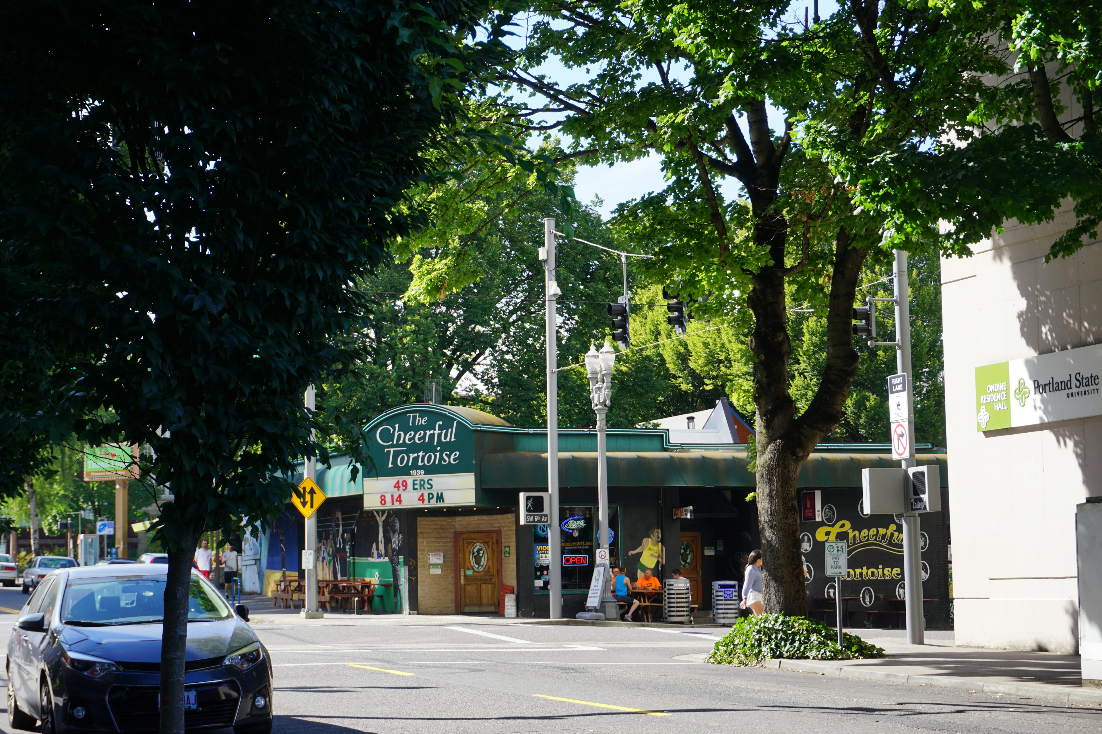 A vibrant street scene featuring a small shop surrounded by trees and parked cars