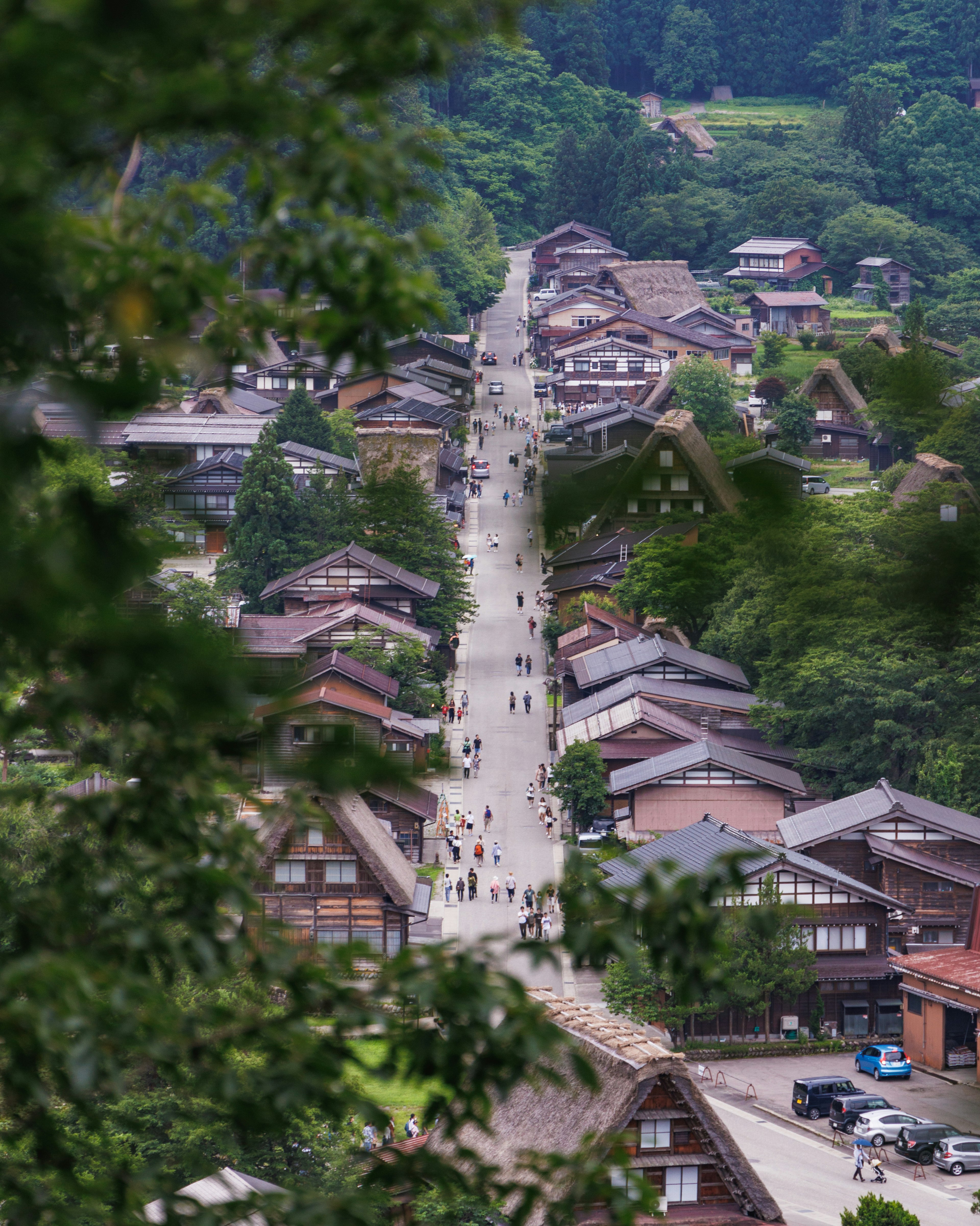 山間傳統村落的風景，行人在小道上，古老的房屋被鬱鬱蔥蔥的綠樹環繞