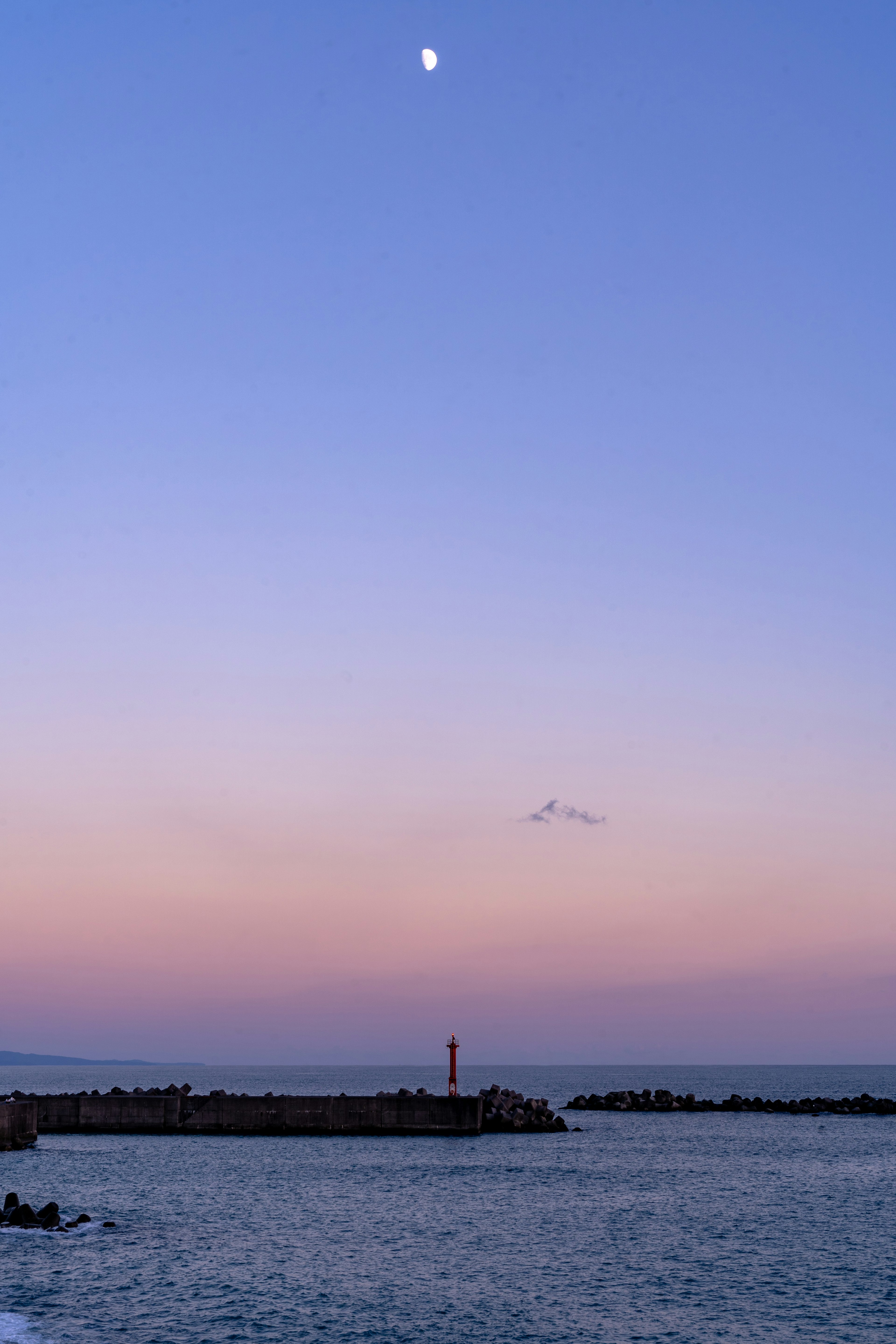 夕焼けの空に浮かぶ月と灯台のシルエット