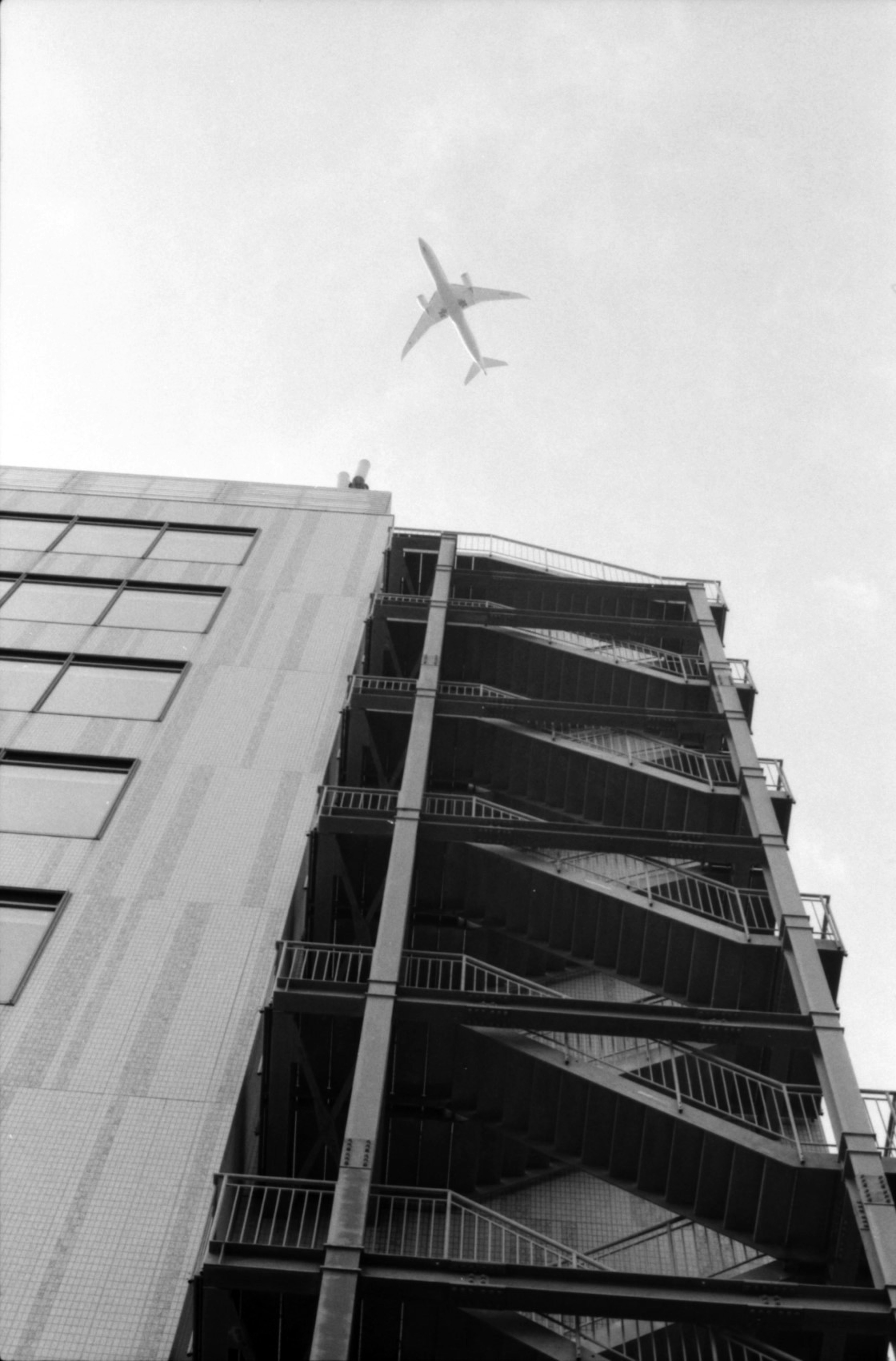 Black and white image of an airplane flying above a high-rise building