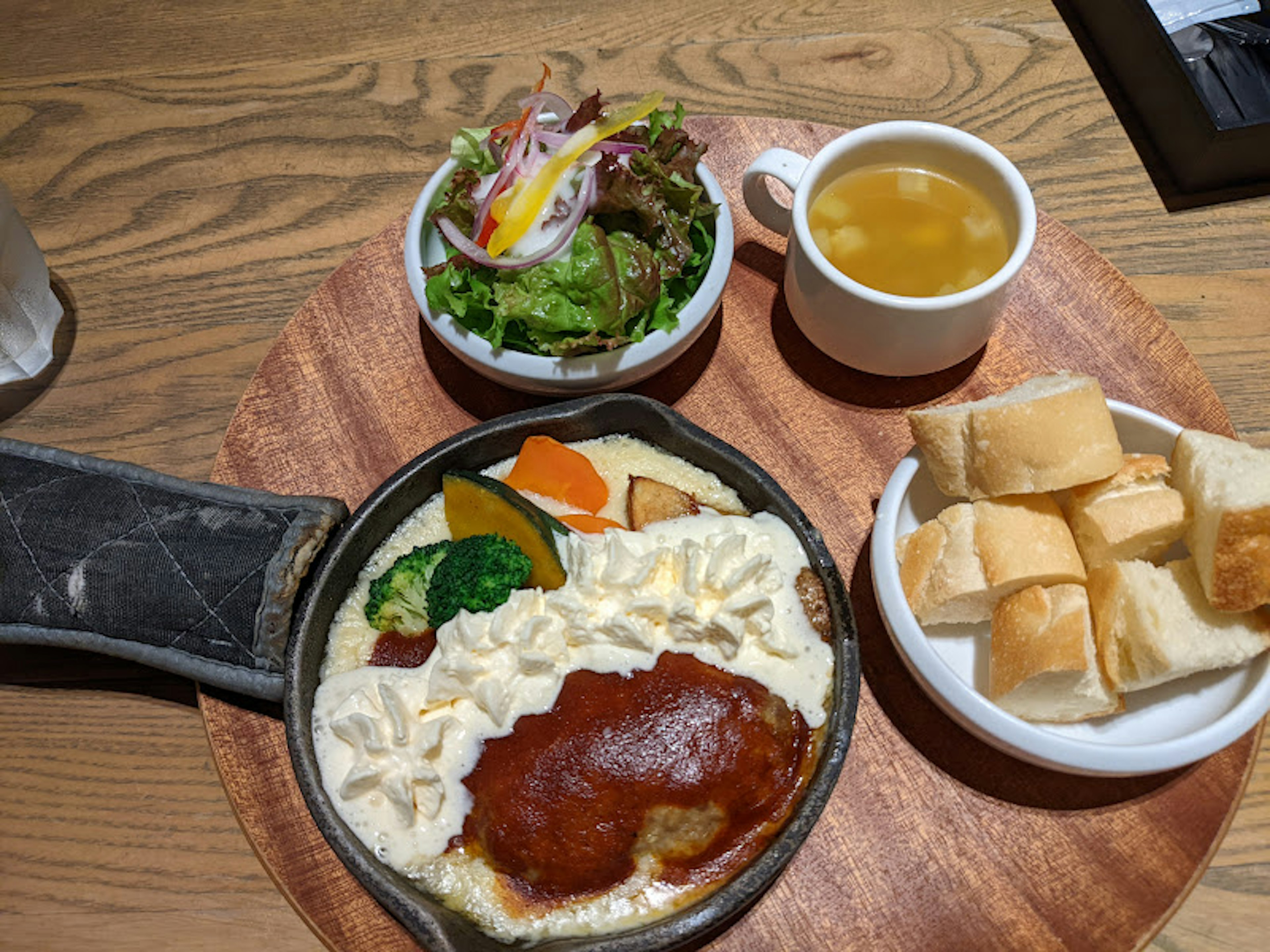 サラダ、スープ、パンとともに提供された熱々のハンバーグと野菜の皿