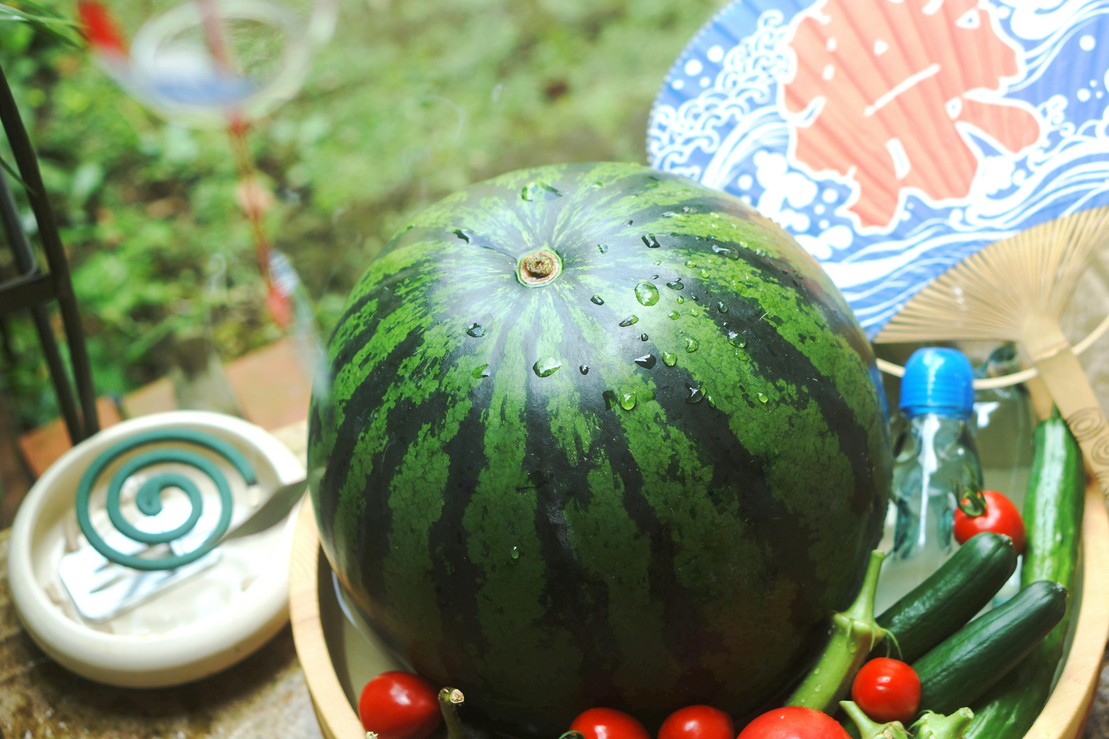 Una sandía verde colocada sobre una mesa de madera rodeada de tomates cherry y pepinos