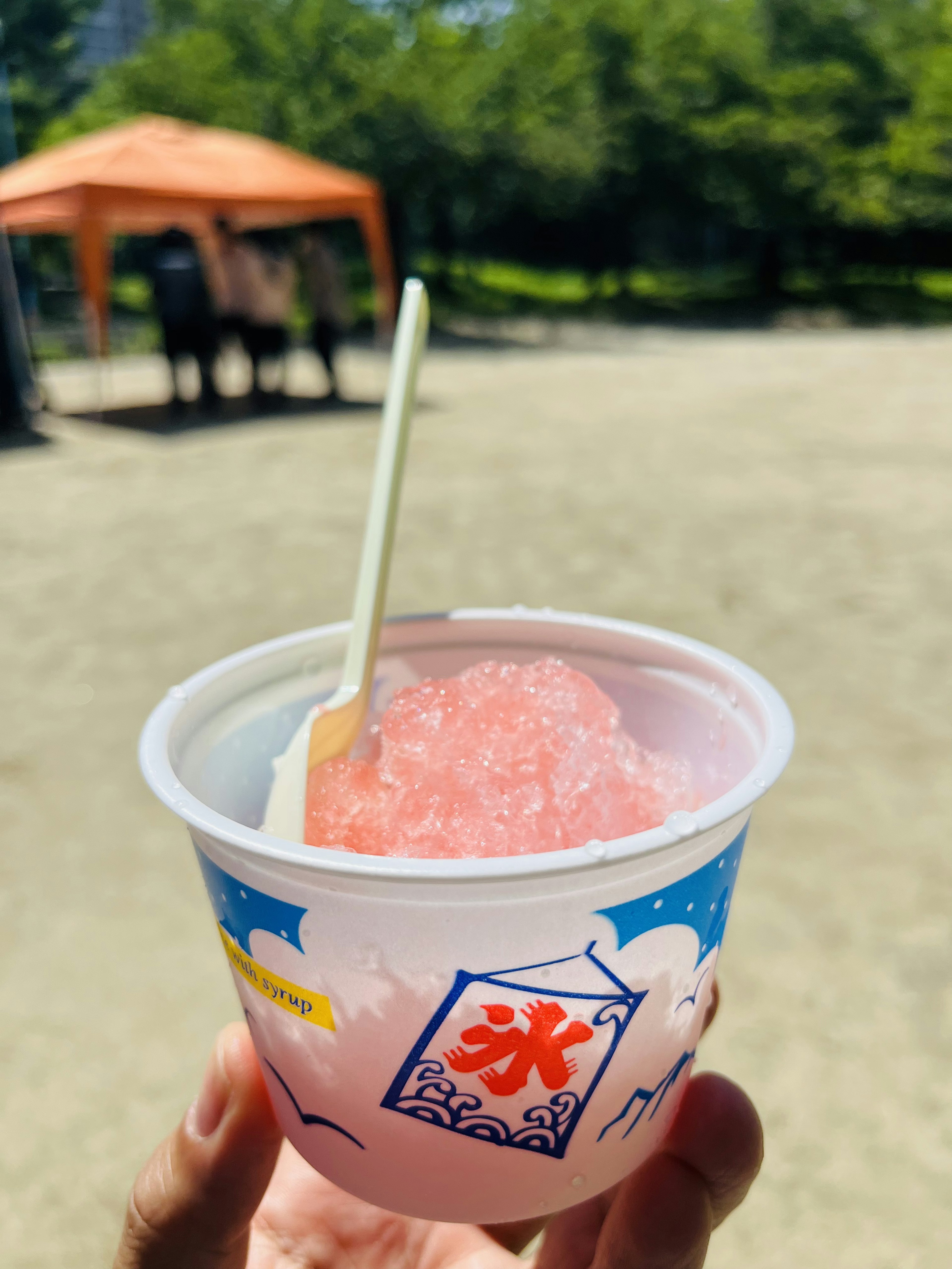 A cup of pink shaved ice with a white spoon