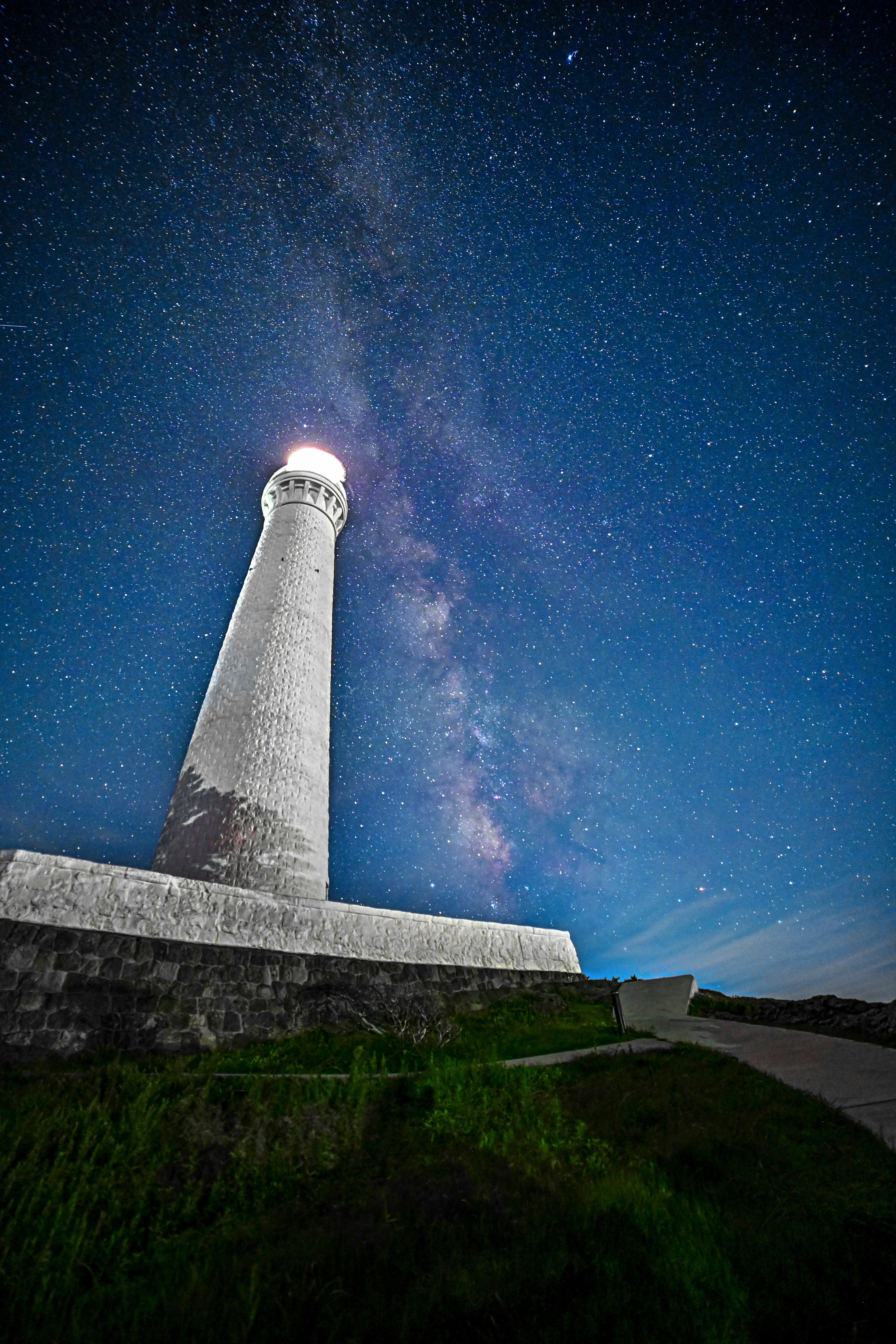 Un faro bajo un cielo estrellado con una impresionante vista de la Vía Láctea