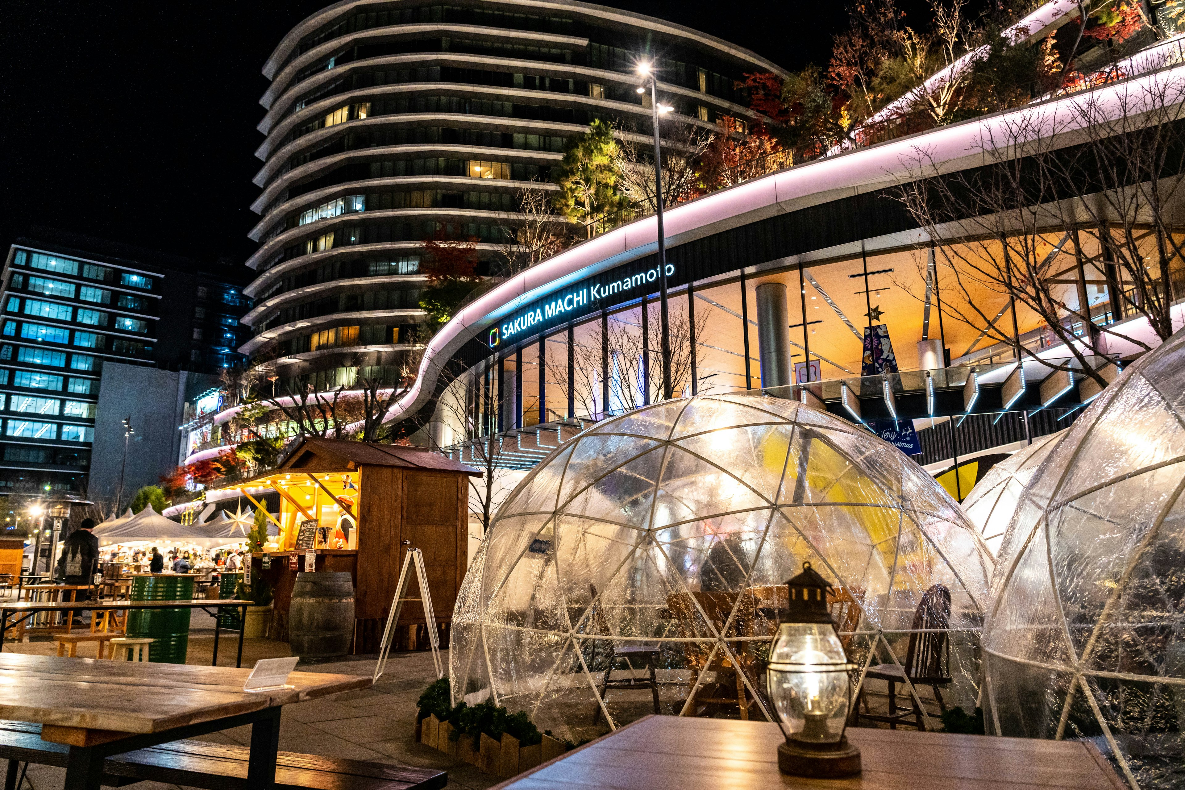 Escena urbana nocturna con terrazas en forma de cúpula transparente y un edificio moderno