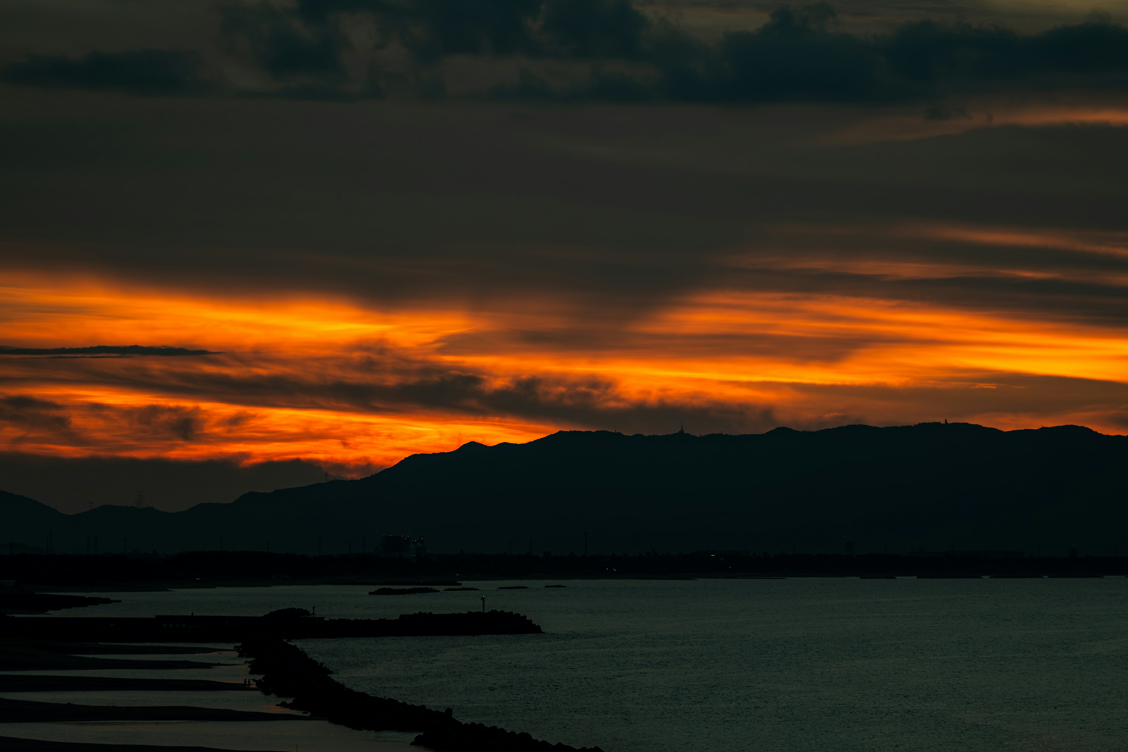 Vista escénica de un atardecer con tonos naranjas en el cielo y silueta de montañas sobre el agua