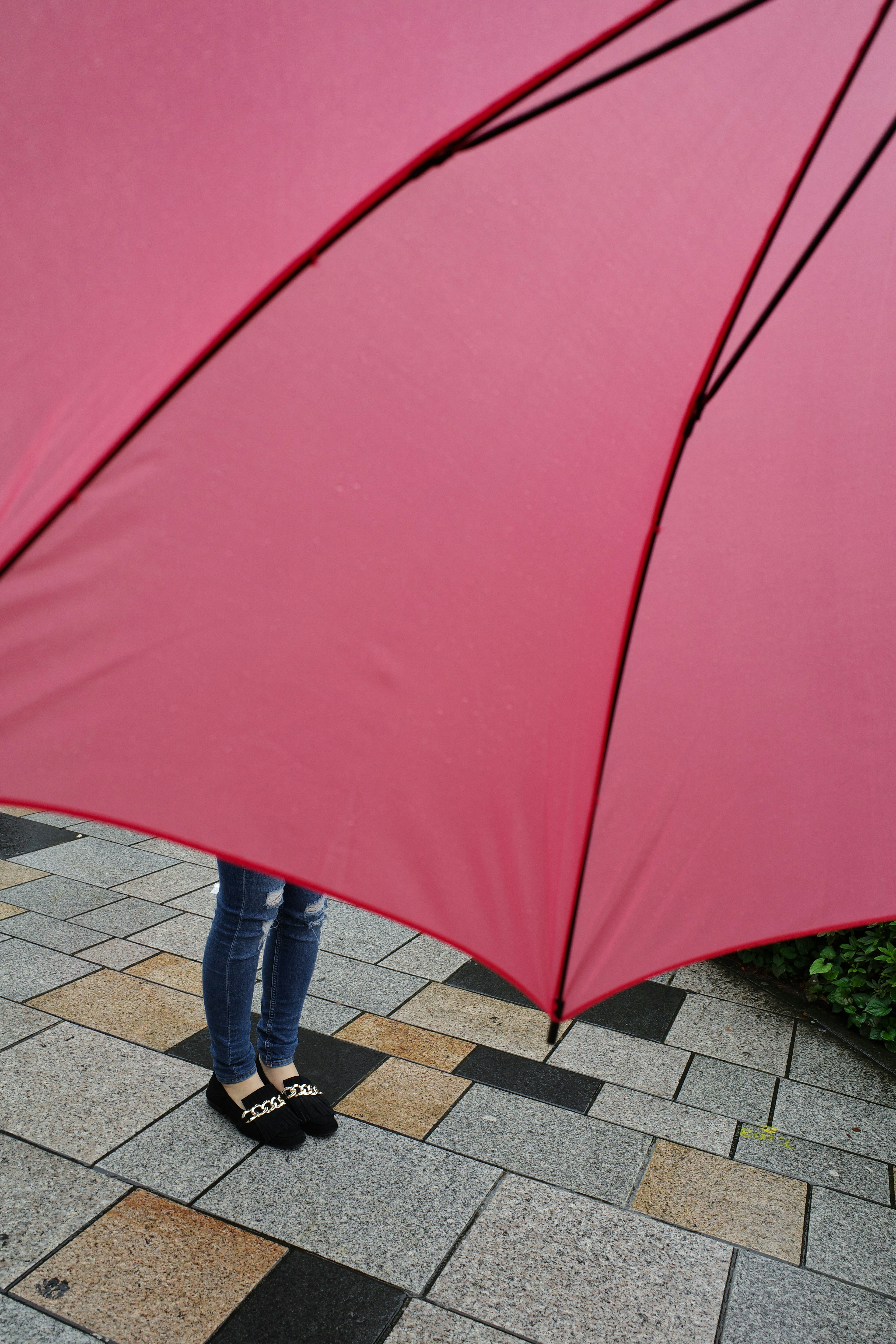 赤い傘の下に立つ女性の足元の部分が見える