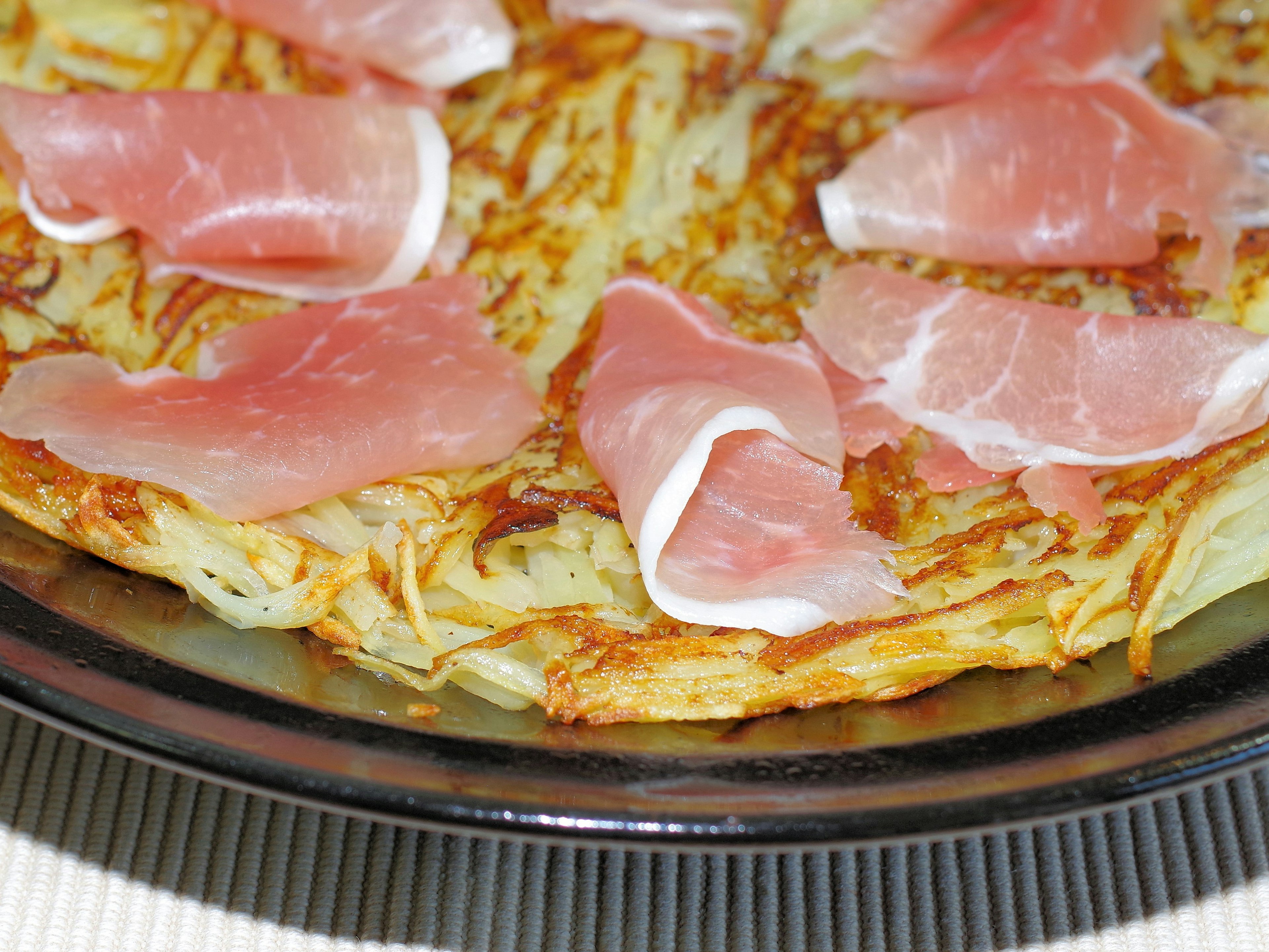 Hash brown dish topped with slices of prosciutto