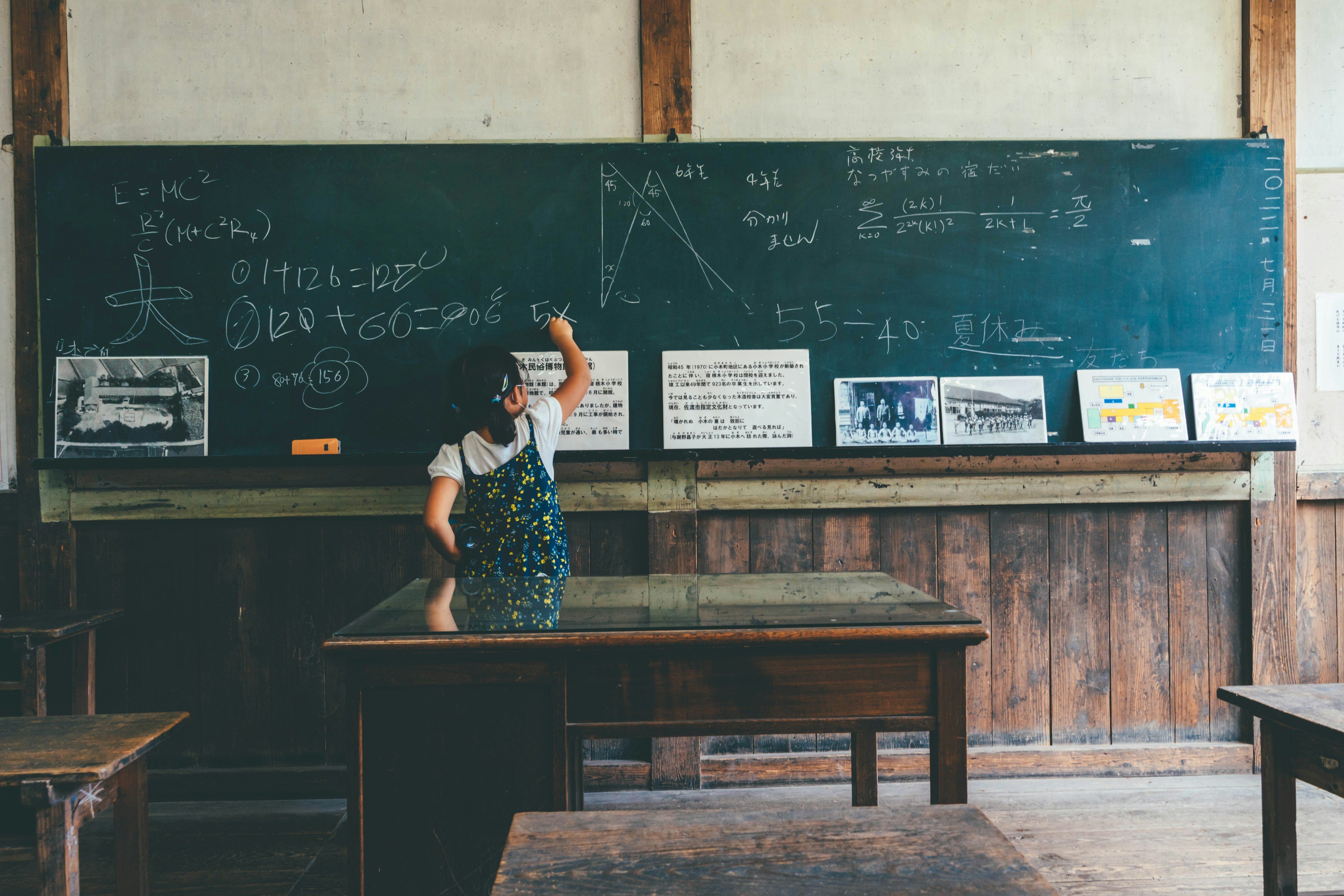 A woman standing in front of a chalkboard in a classroom with wooden desks